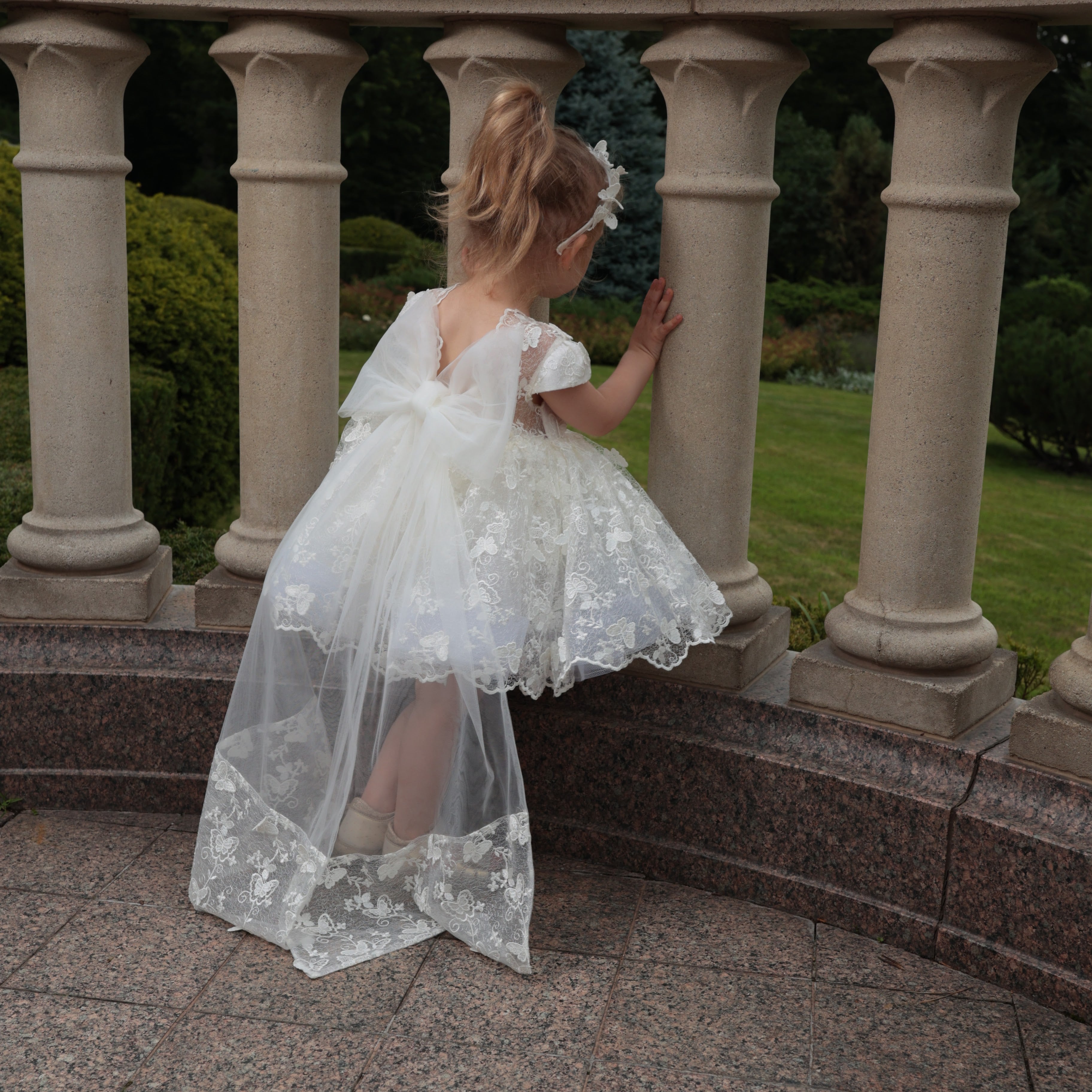 Young girl in a white lace dress standing on a stone staircase with columns.