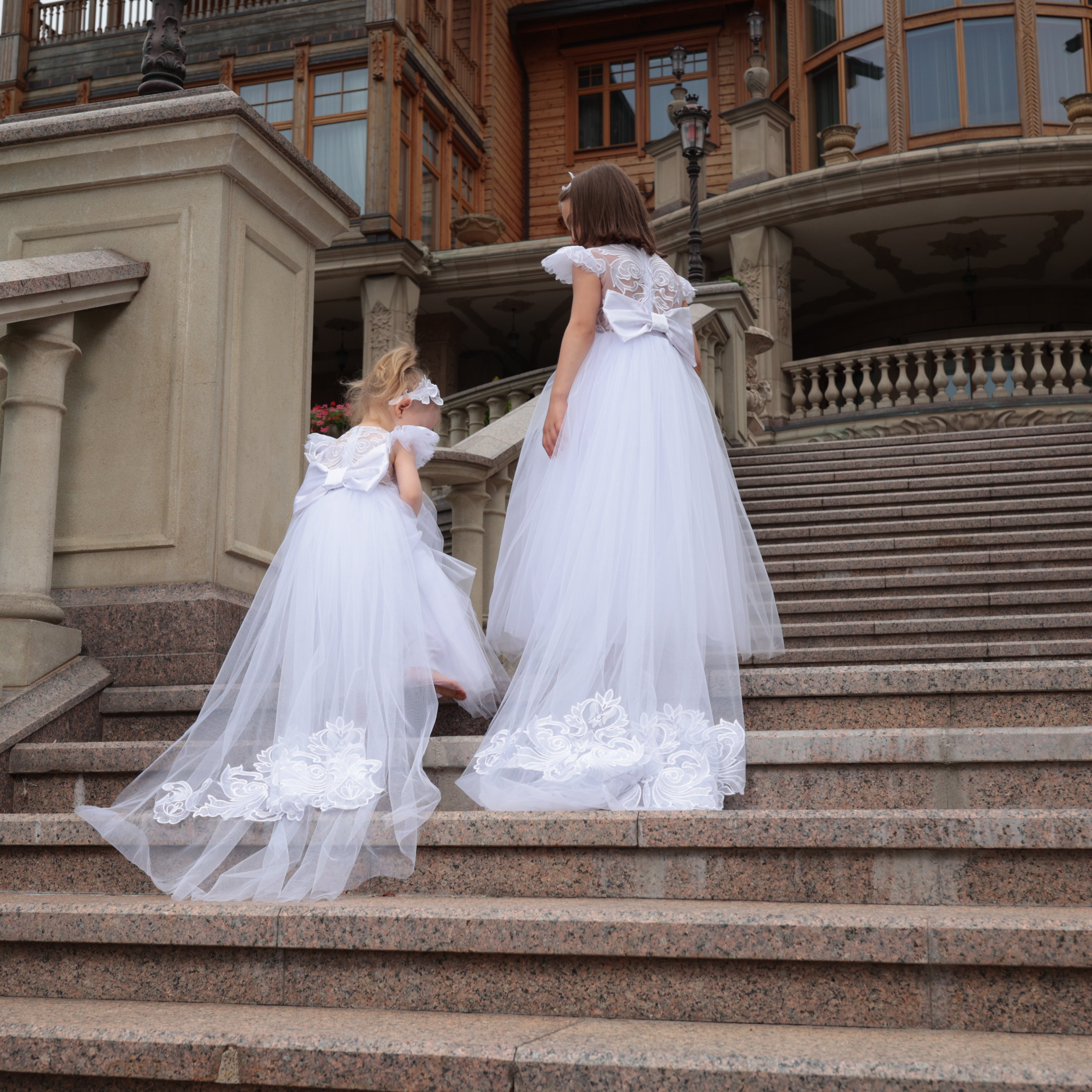 Two women in white dresses standing on stone steps of a large building.