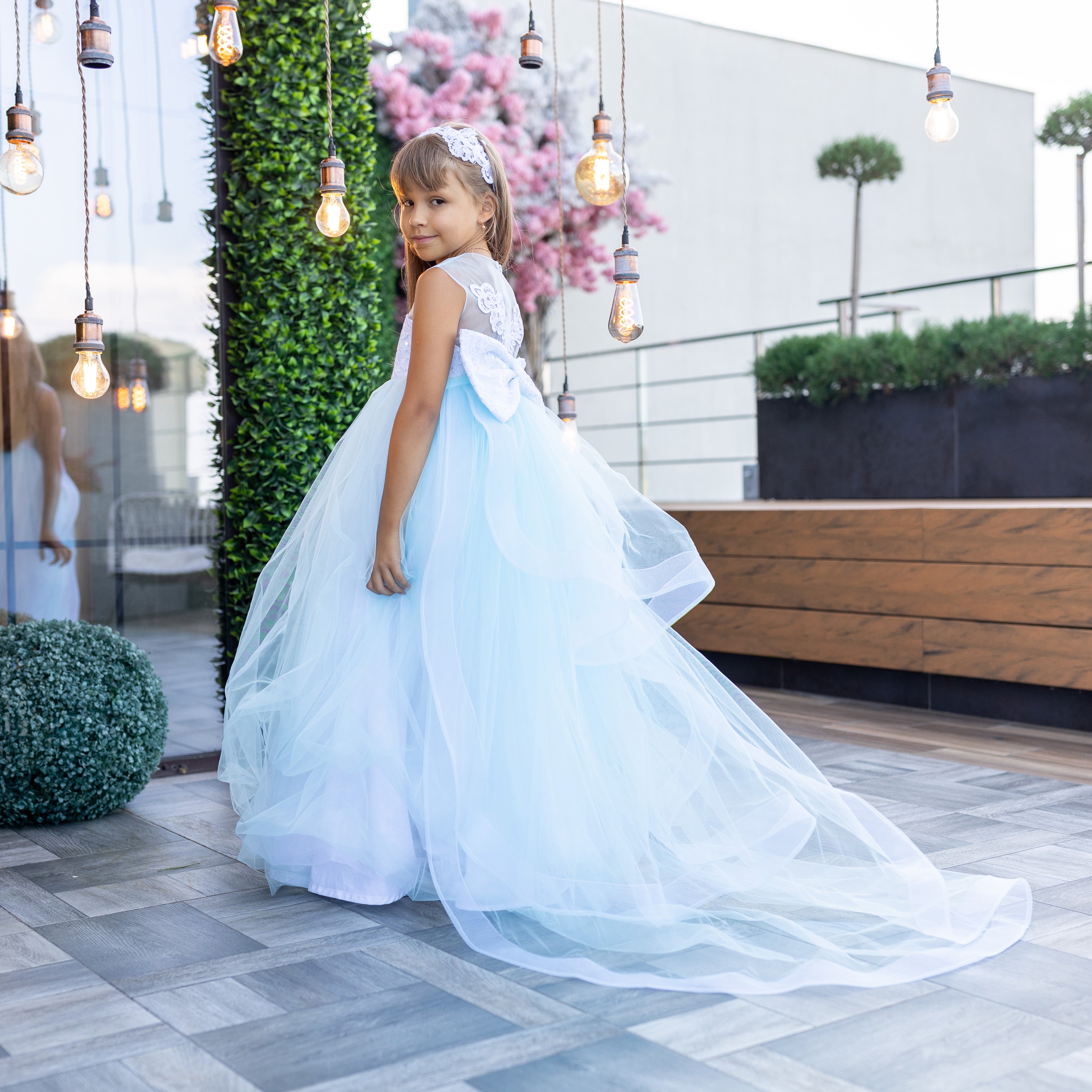 Young girl in a white dress standing on a rooftop with modern decor and plants.