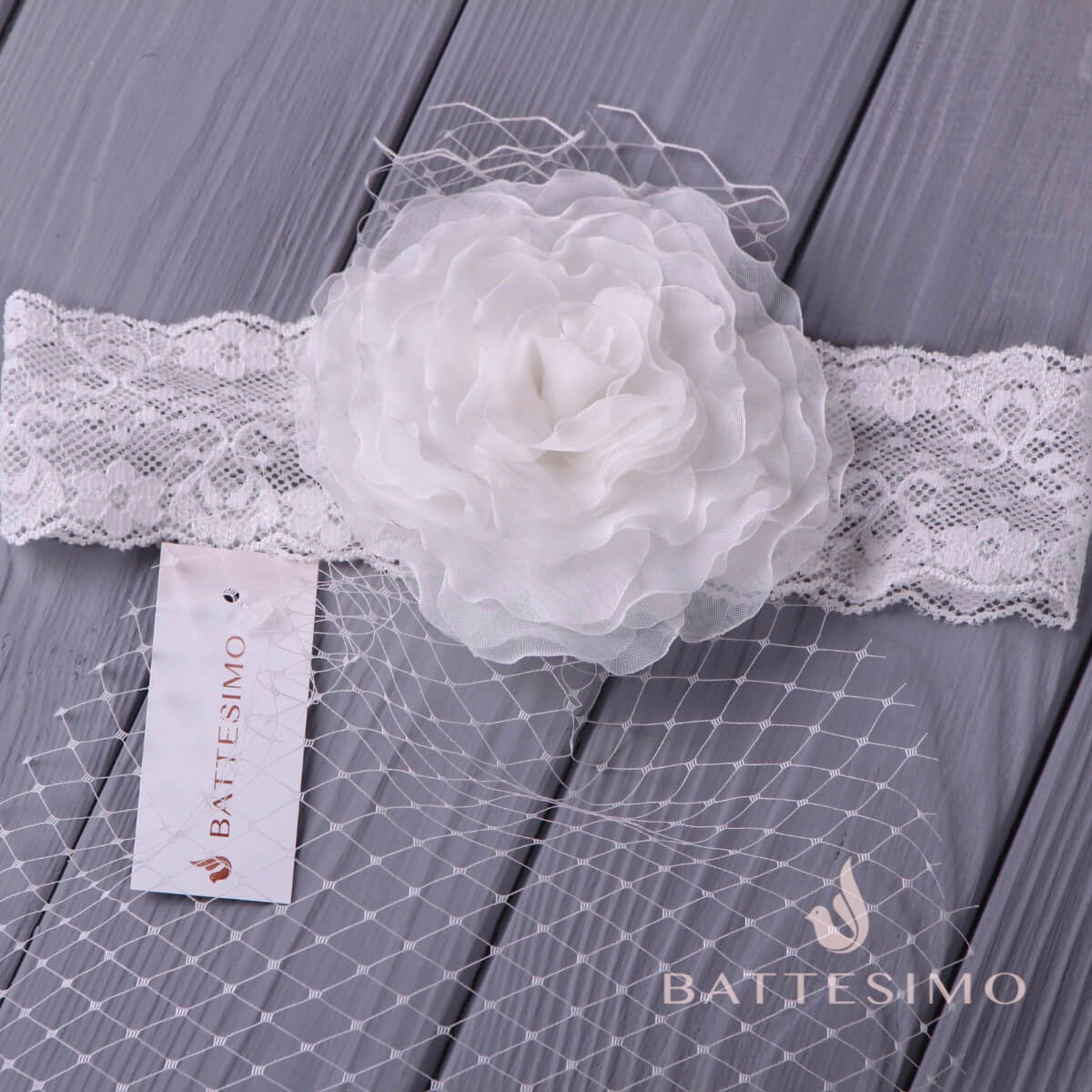 Baby headband with floral detail on a gray wooden surface, featuring the Battesimo brand.
