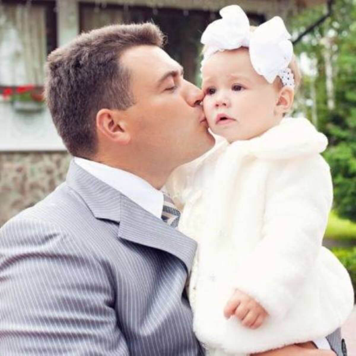 Man kissing a baby , wearing  Baby Keepsake Fur Coat with Hat on the cheek outdoors