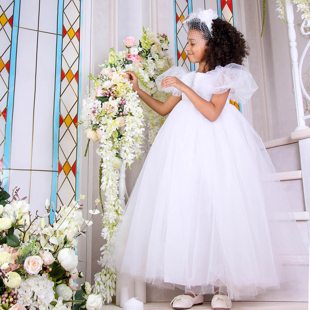 Young girl in a white dress standing next to floral decorations in a church setting