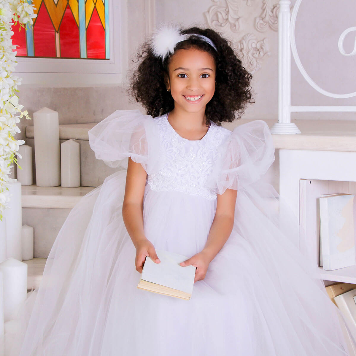 Young girl in a white dress holding a book, sitting on a decorative step.