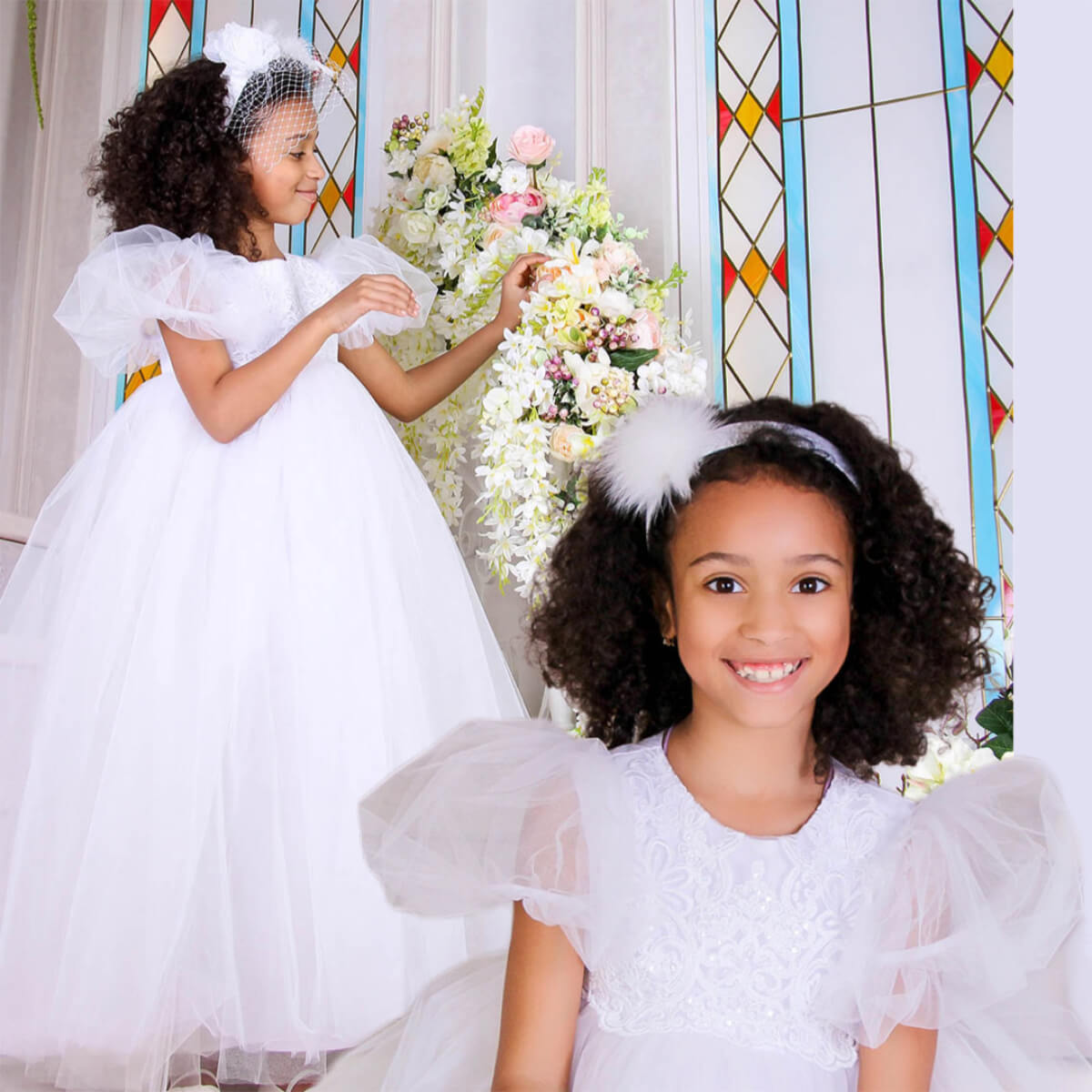 Two young girls in white dresses standing in front of a floral arrangement and stained glass window.