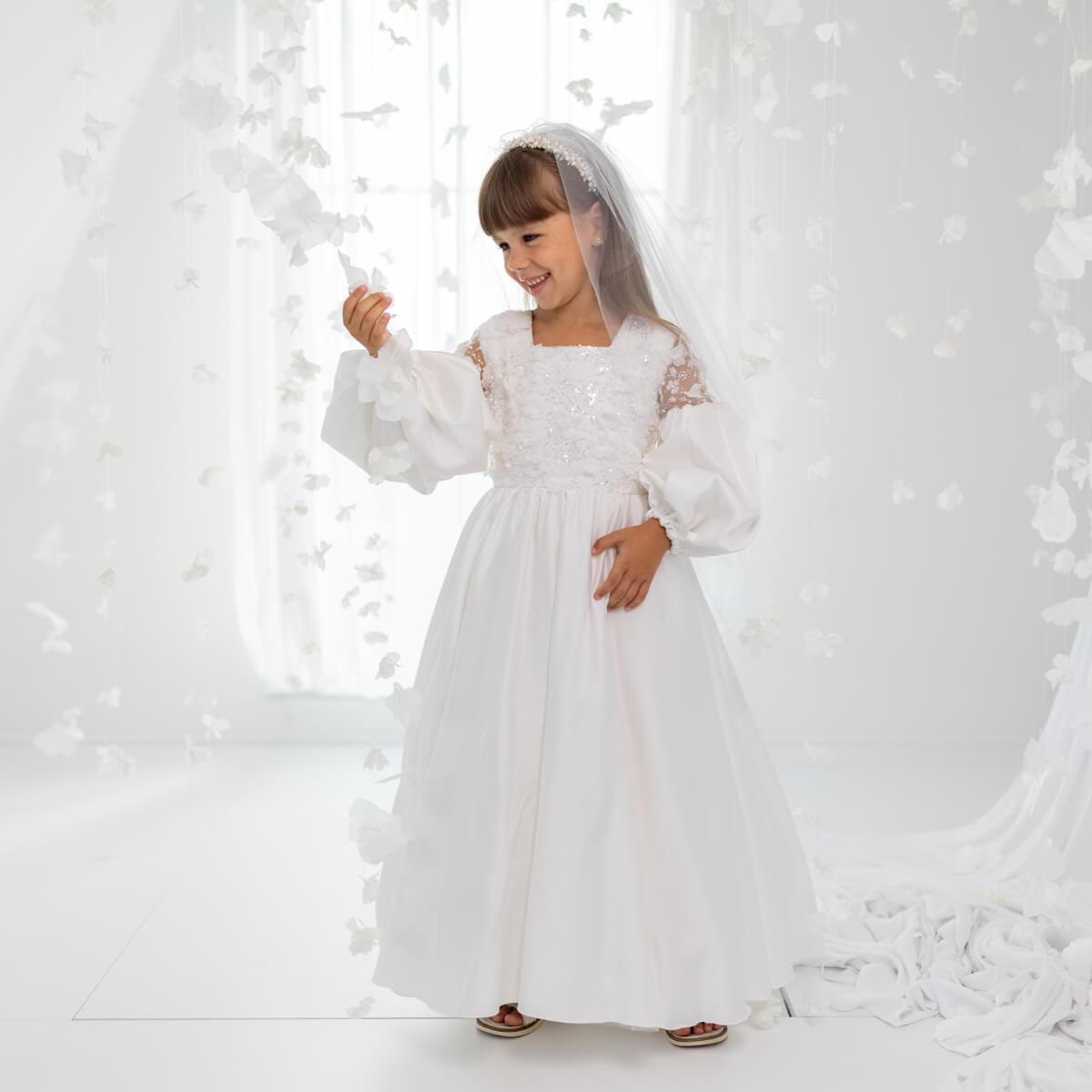Young girl in a Silk First Communion Dress with a veil standing against a snowy background