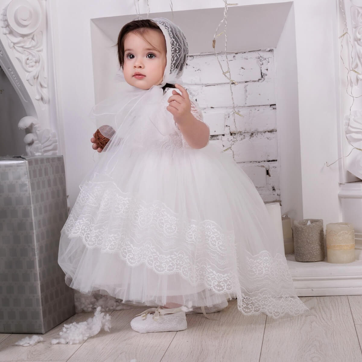 Child in a Baptism Dress with Train standing in a decorated room.