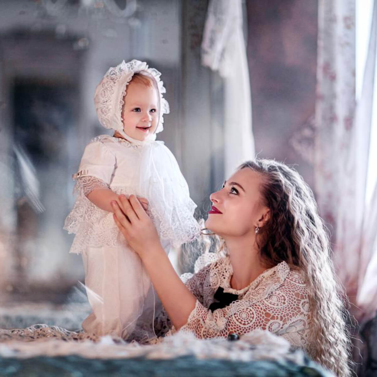Woman holding a baby dressed in white christening romper with a blurred background
