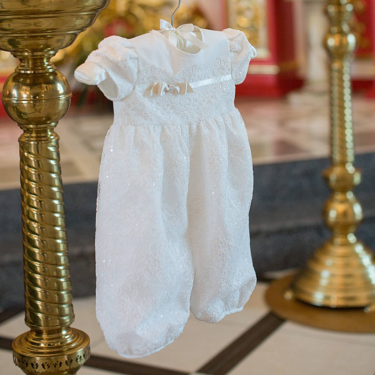 Baptism bubble romper hanging between two gold candle holders with a blurred background