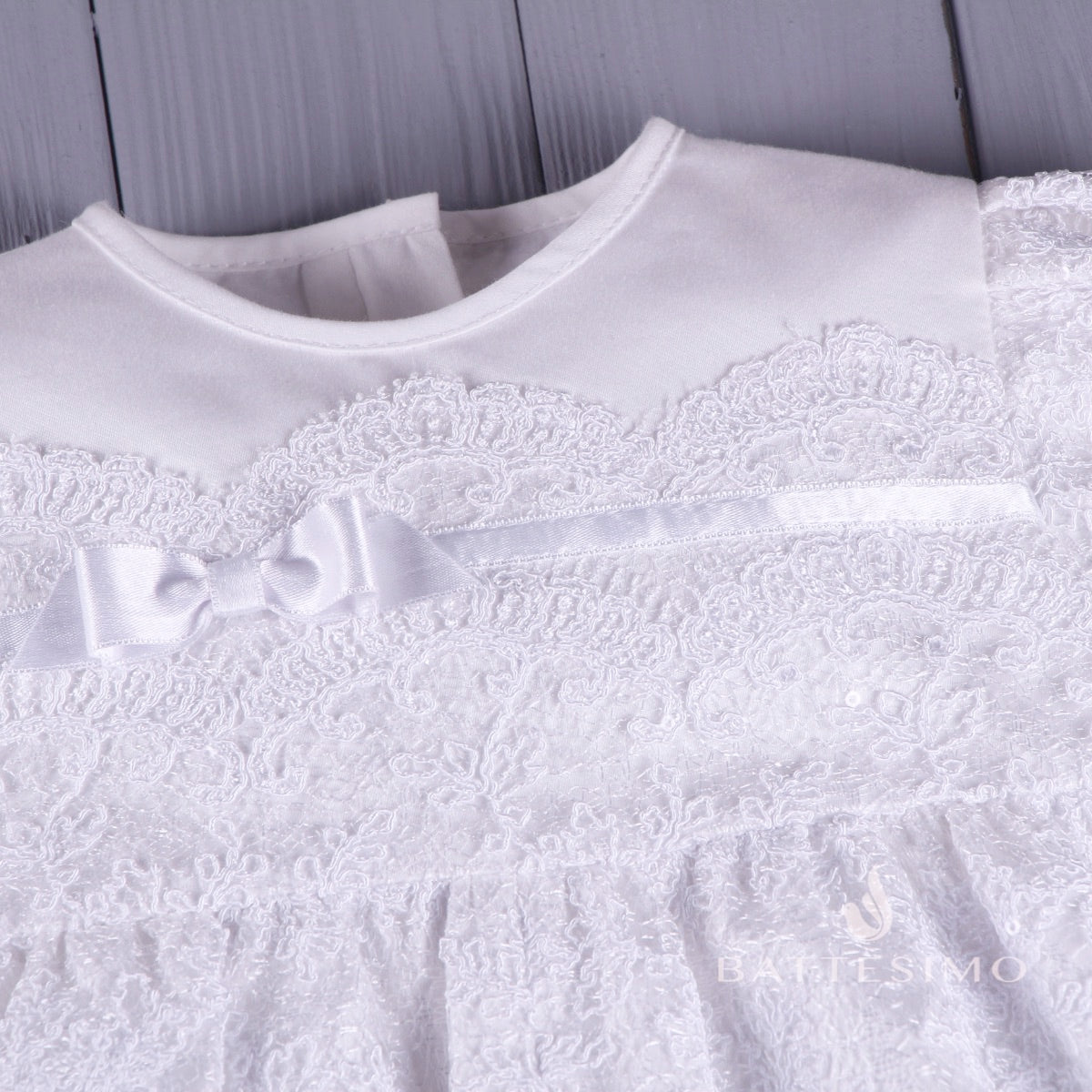 Baptism bubble romper with a bow detail on a textured gray background