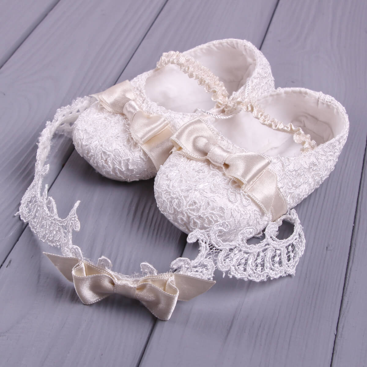 White lace baby shoes with baby headband  on a gray wooden surface