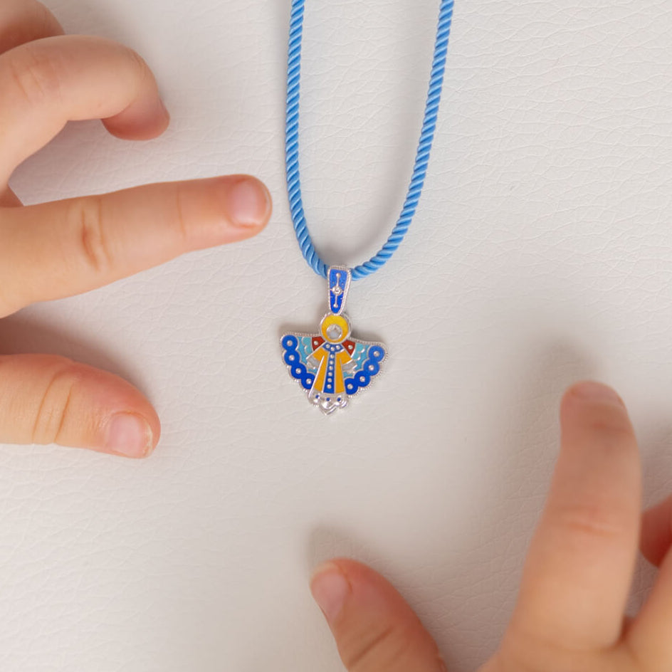 Child's hand reaching towards a blue necklace with an angel pendant on a white background