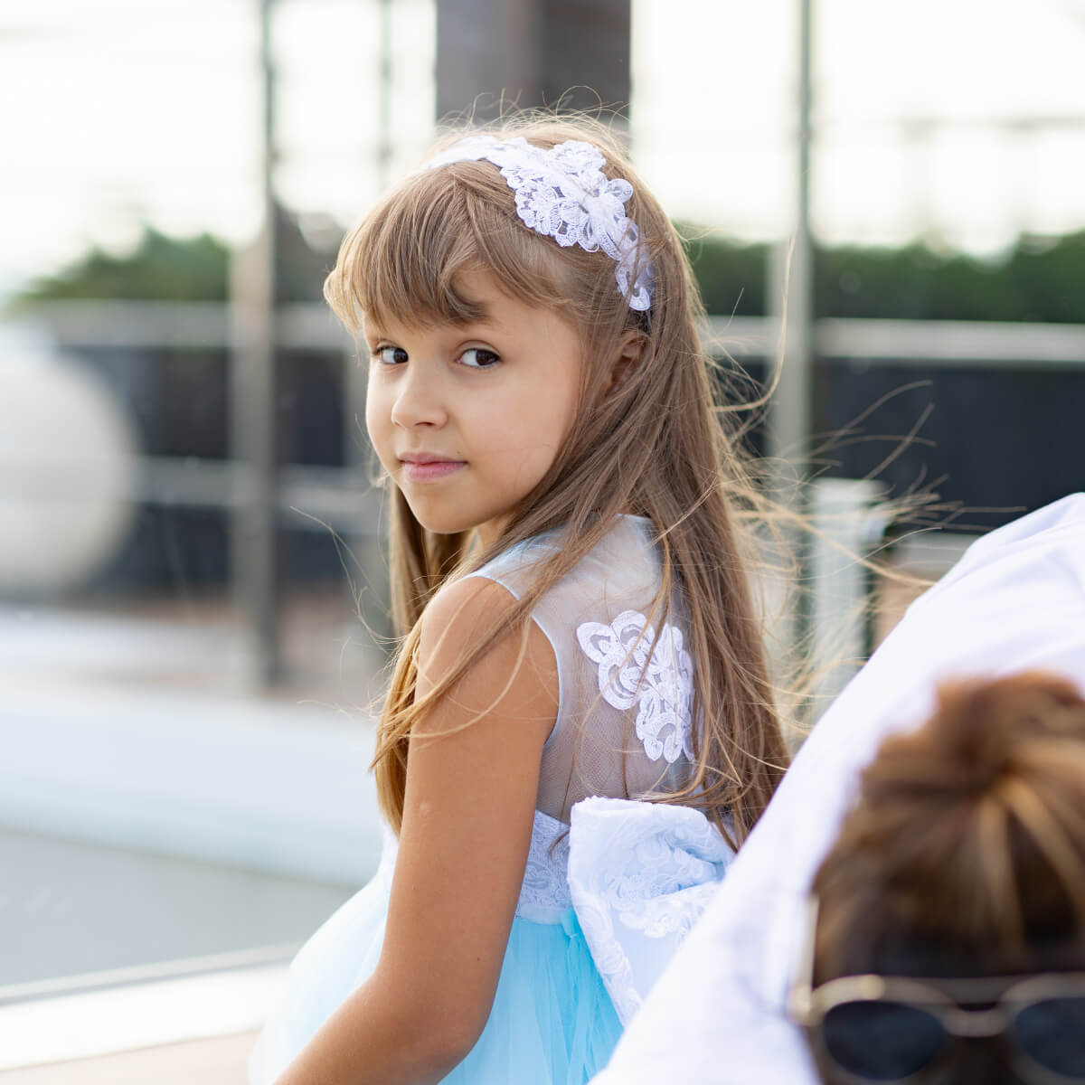 Young girl in a light blue flower girl dress with a white floral headband, sitting outdoors.