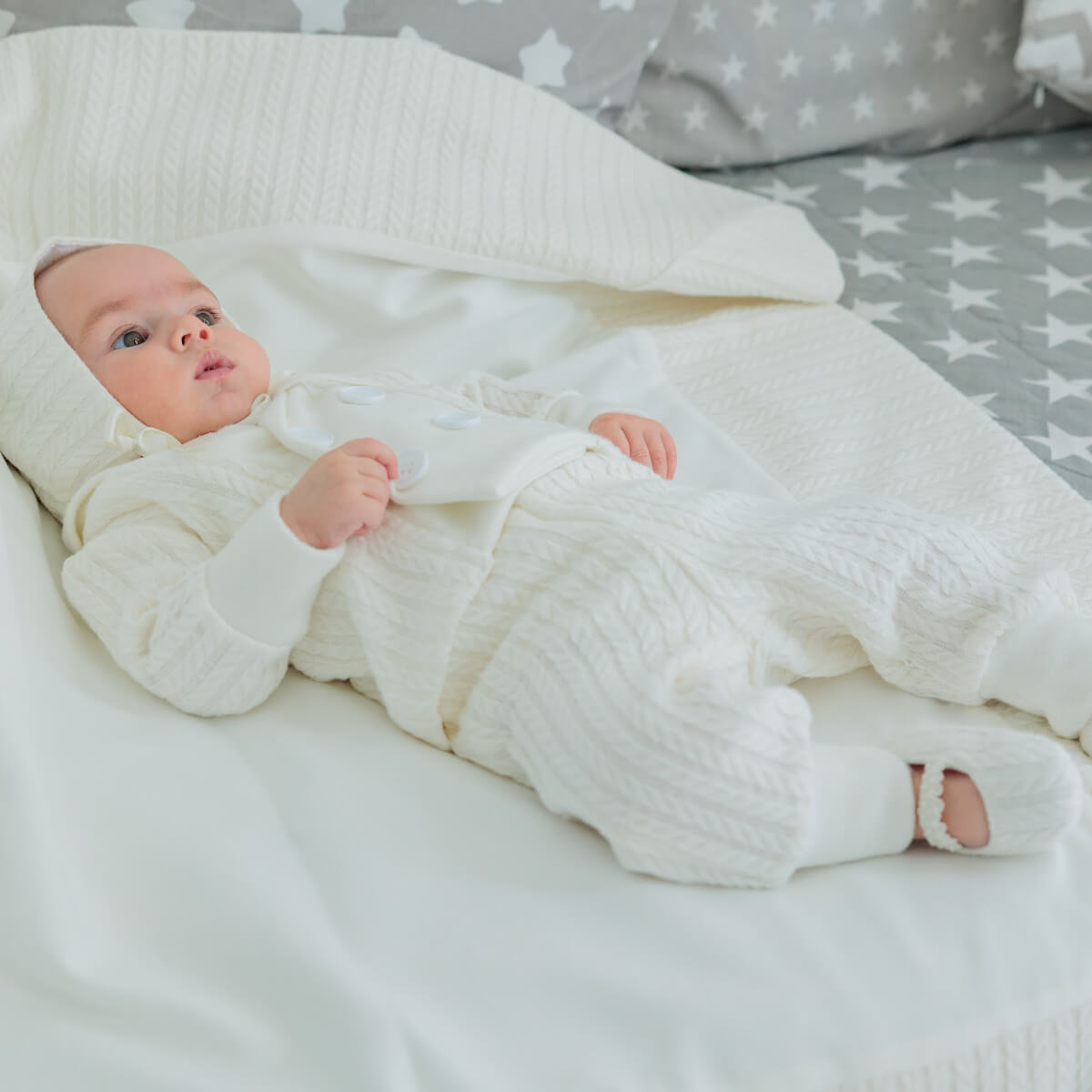Child in a Baby Boy Christening Suitl lying on a bed with a gray star-patterned blanket.