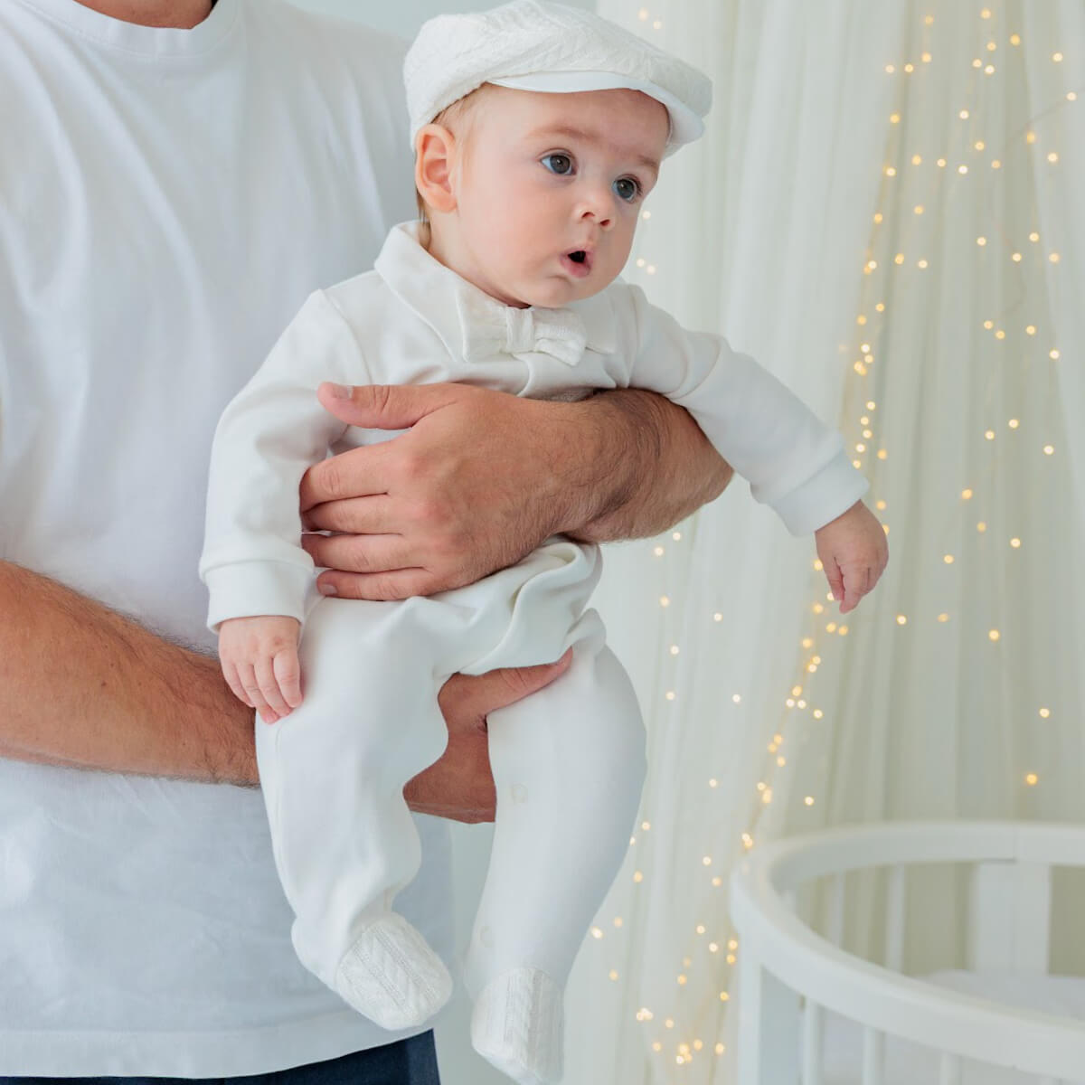 Baby in a Coming Home Jersey Outfit being held by an adult in a softly lit room with fairy lights.