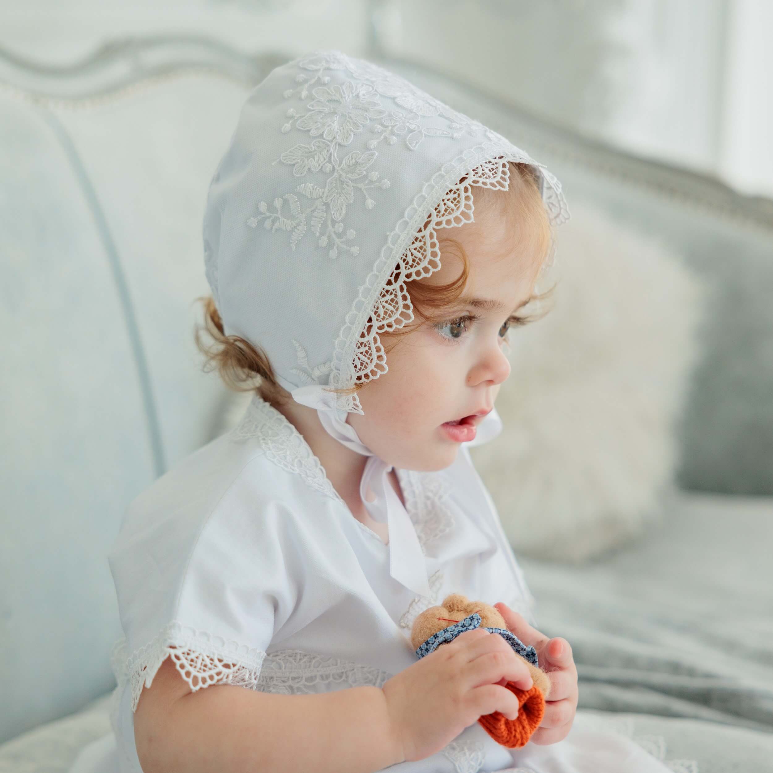 Child wearing  Lace Baptism Bonnet sitting on a couch.