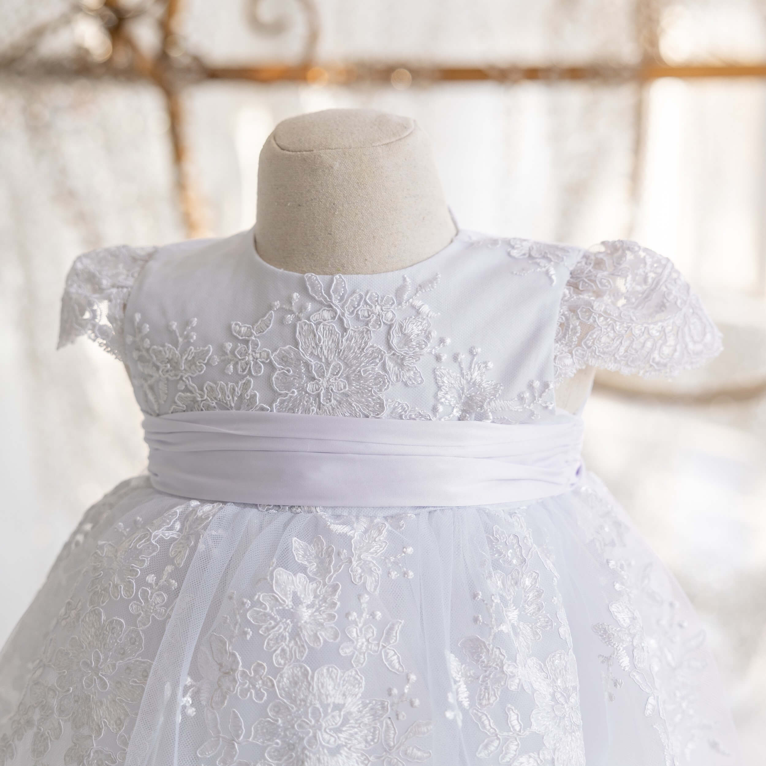 Lace Baptism Dress on a mannequin against a blurred background