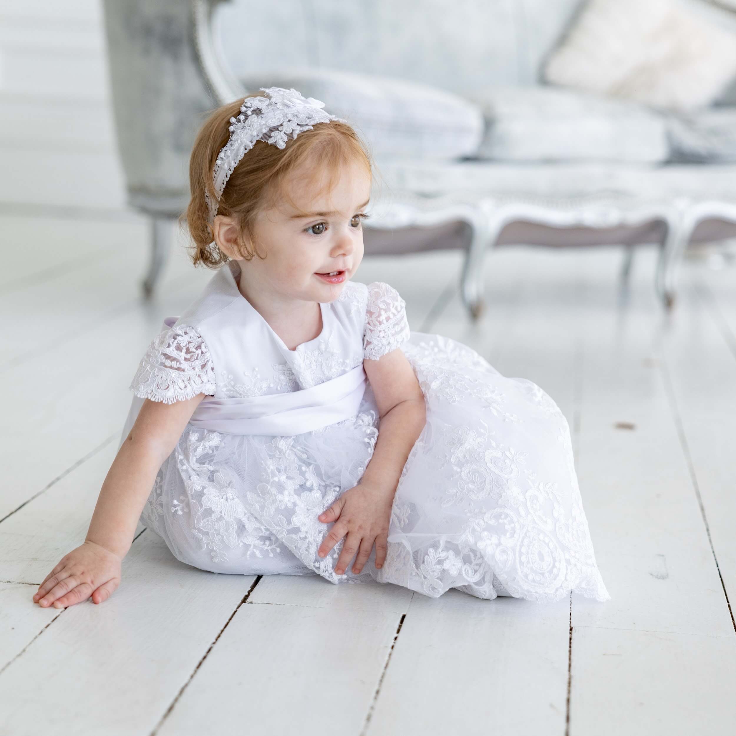Young girl in  baby headband sitting on a light wooden floor.