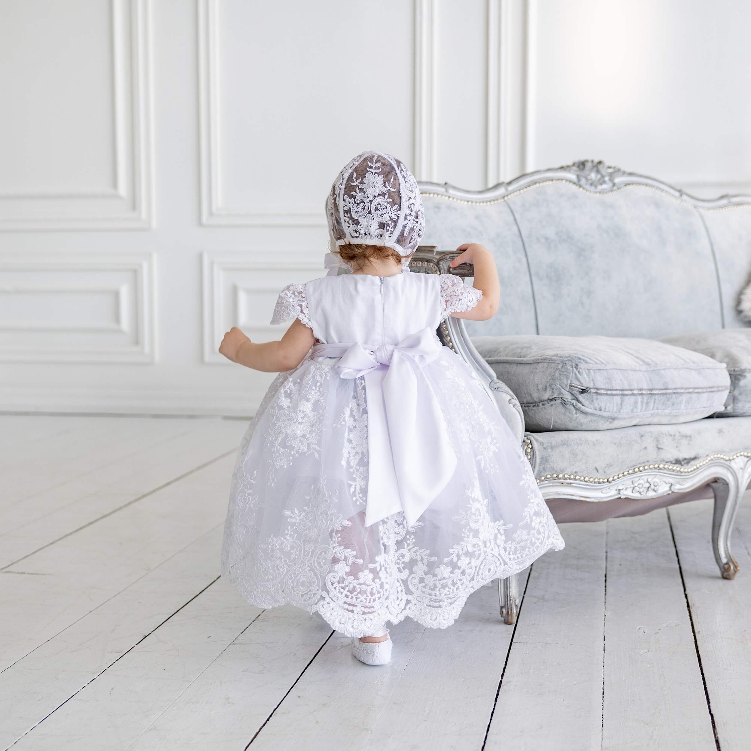 Child in a Baptism Dress Set for Girls  standing in a room with a gray sofa.