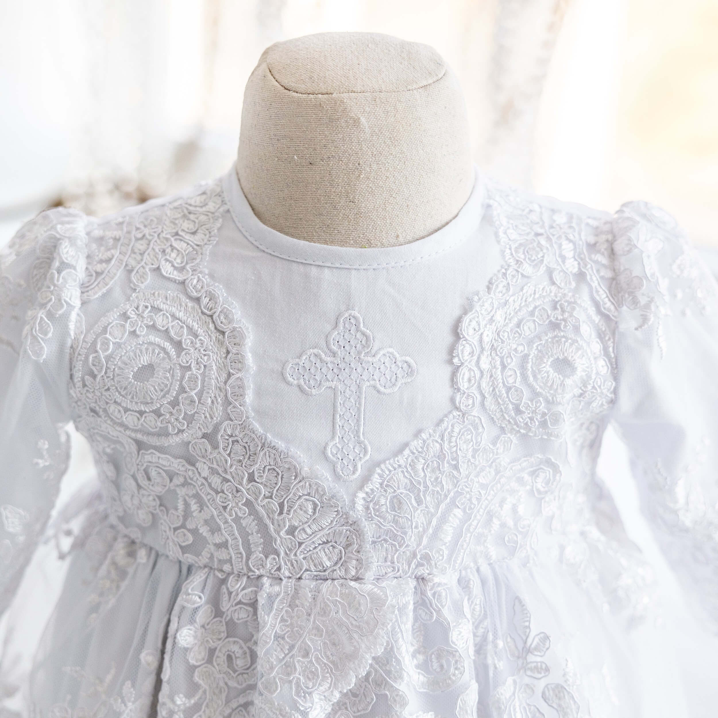 Christening Gown for Girls on a mannequin with a cross design against a blurred background