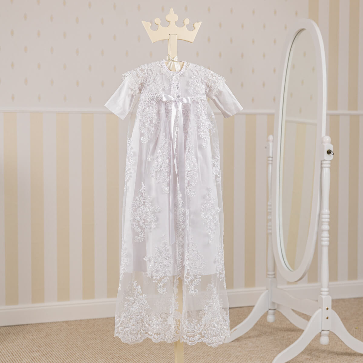 Christening Gown for Girls on a hanger against a neutral wall with a mirror.