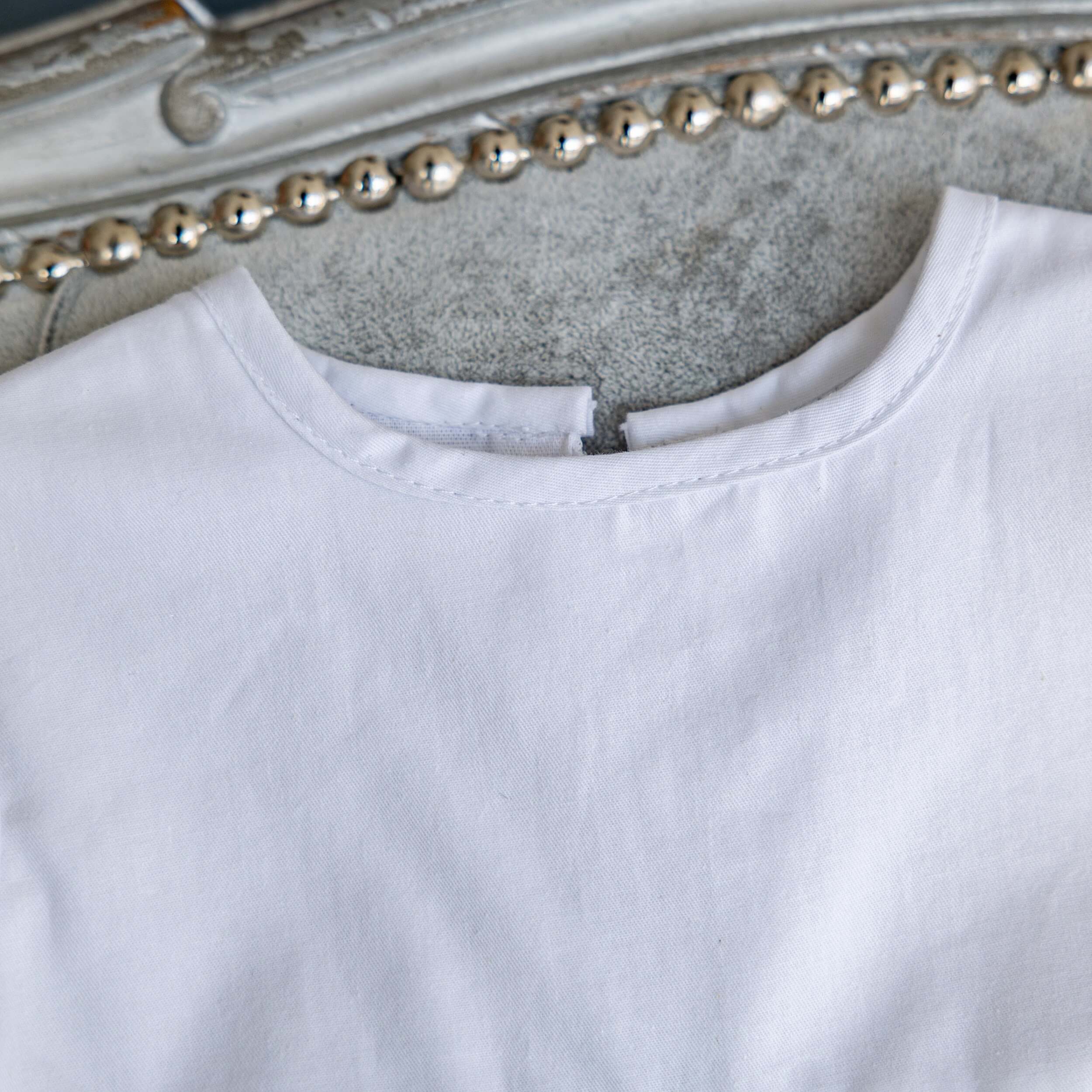 Close-up of a  Christening Gown for Girls  collar with a decorative headboard in the background