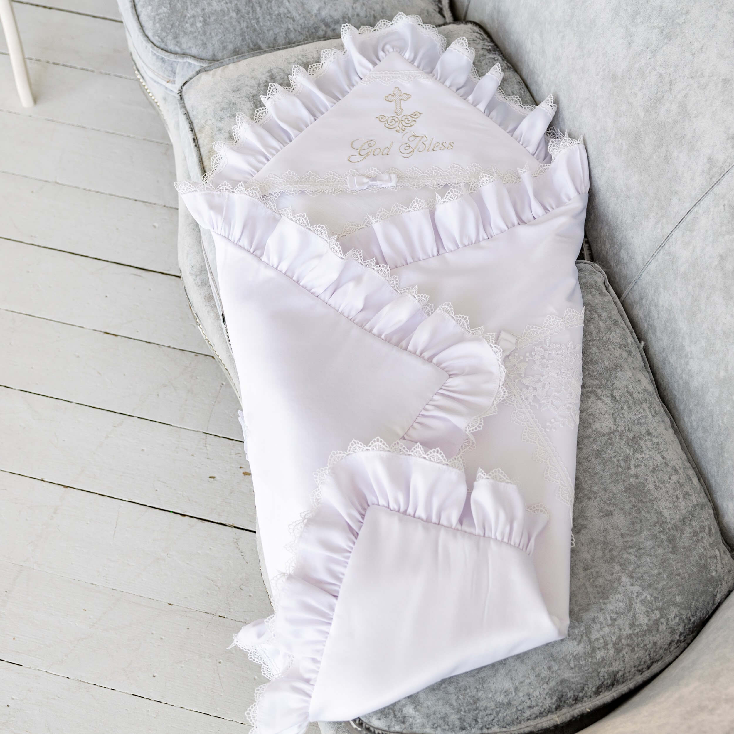 White baby blanket with ruffles and embroidery on a gray chair.