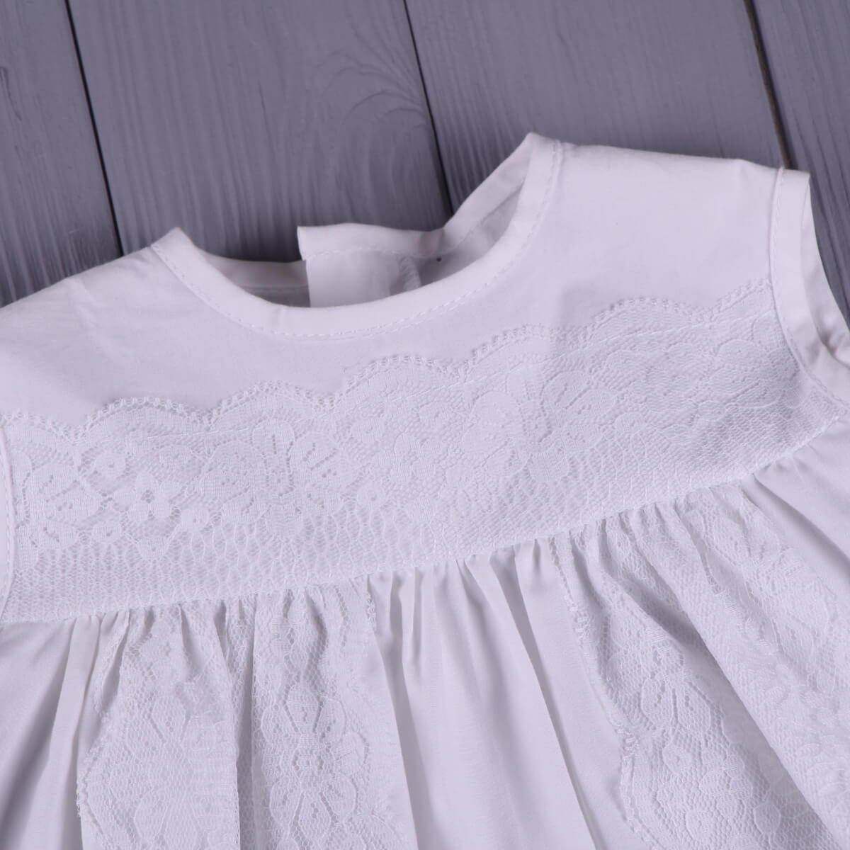 Summer Baptism Dress with lace detailing on a wooden surface