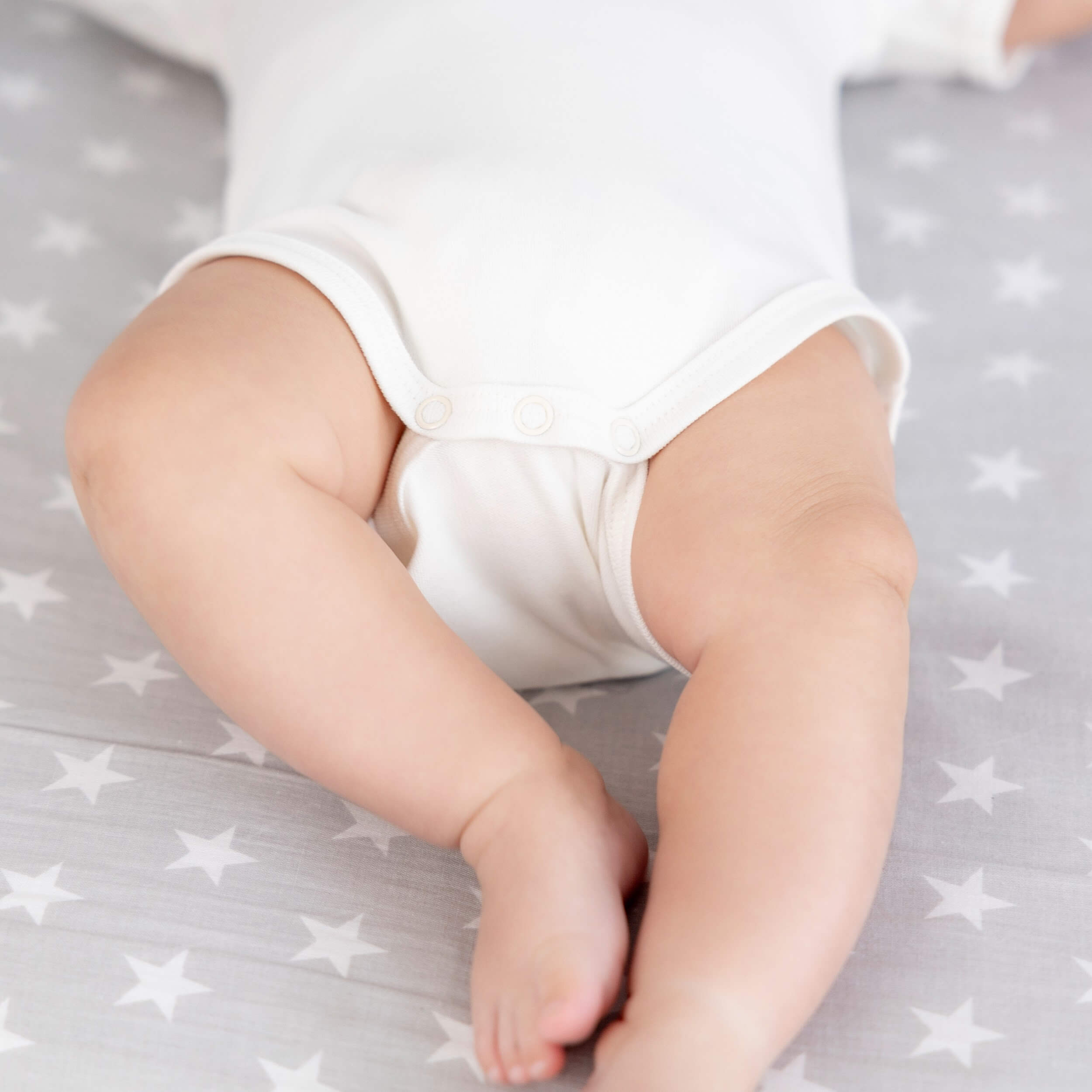 Close-up of a baby's legs in Coming Home Bodysuit  on a gray blanket with star patterns