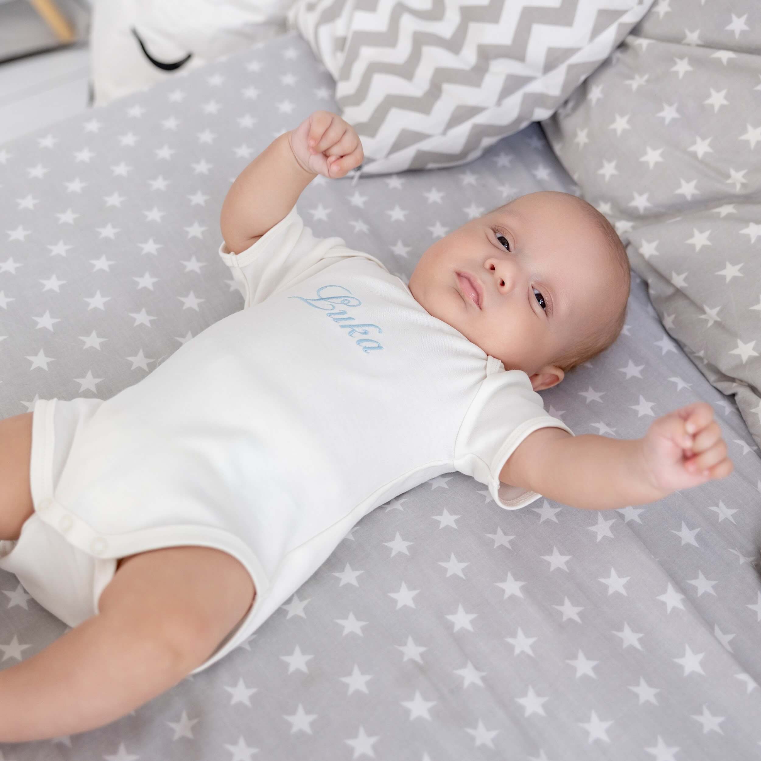 Baby lying on a gray blanket with star pattern, wearing a Coming Home Bodysuit .