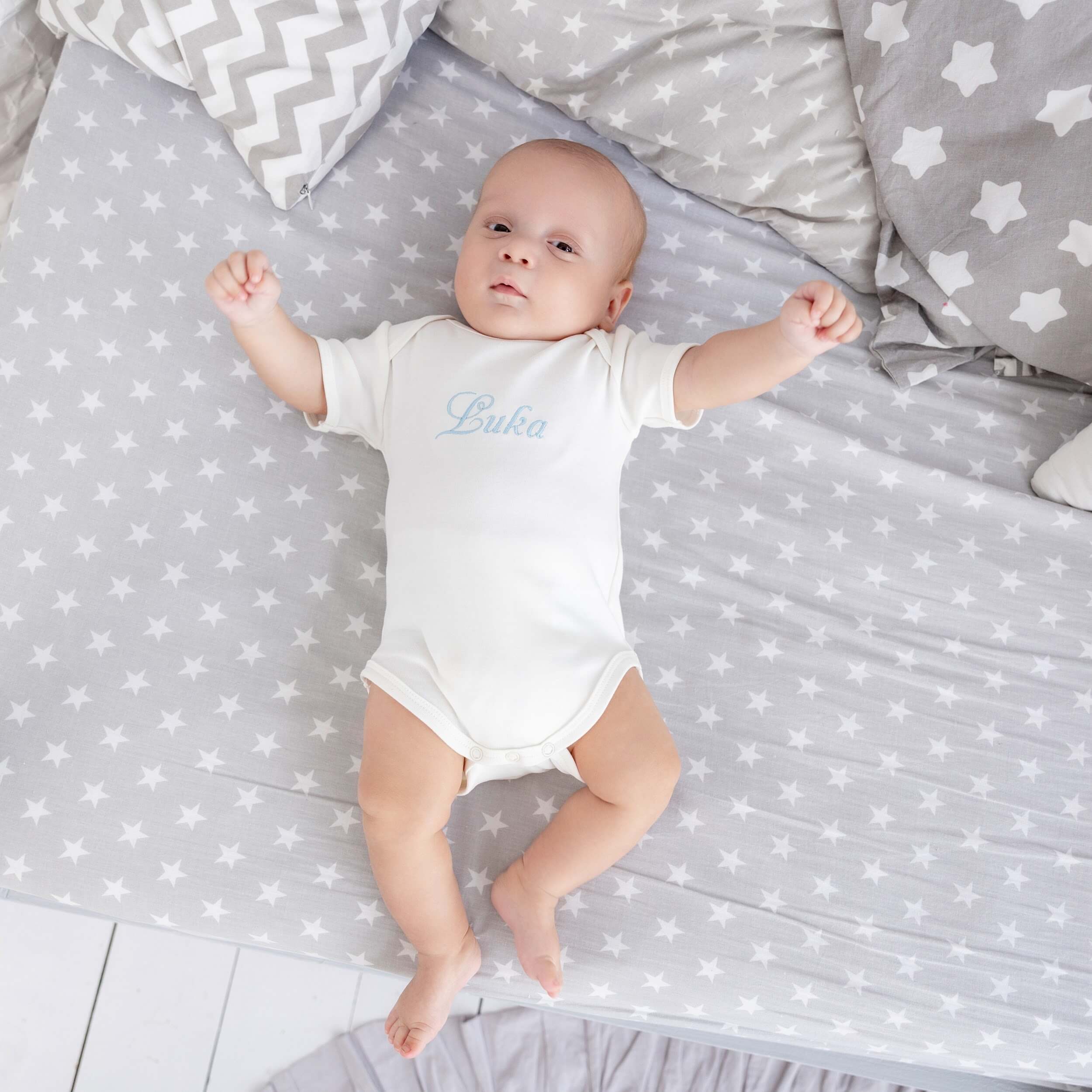 Baby lying on a gray blanket with star patterns, wearing a Coming Home Bodysuit .