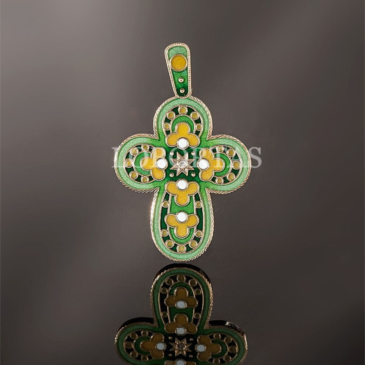 Decorative cross pendant with green and gold colors on a reflective surface.
