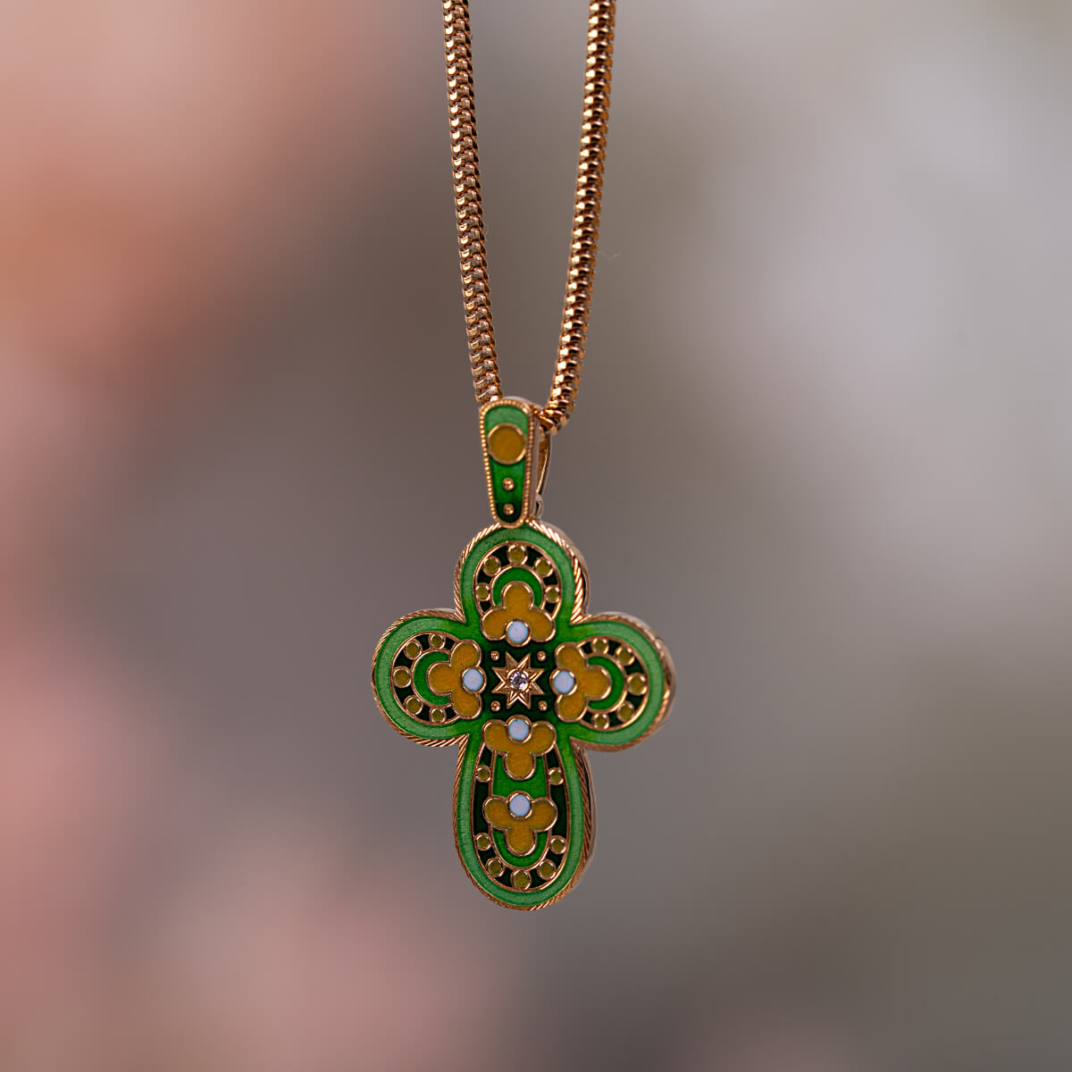 Gold and green cross pendant on a blurred background