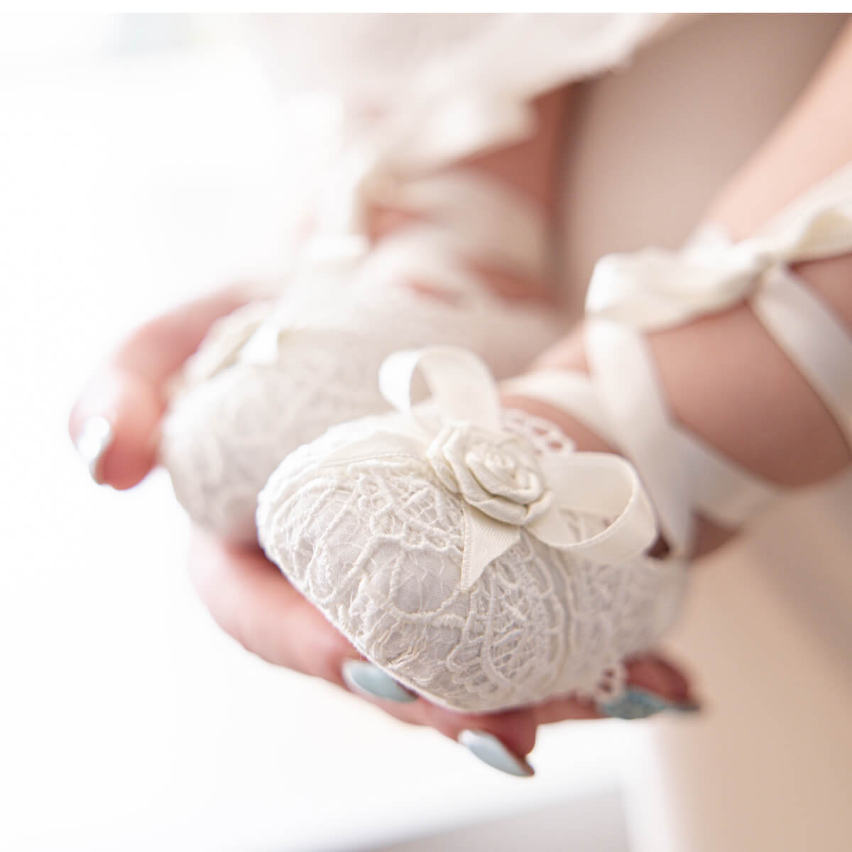 Close-up of a hand holding a small Christening Booties with a flower detail.