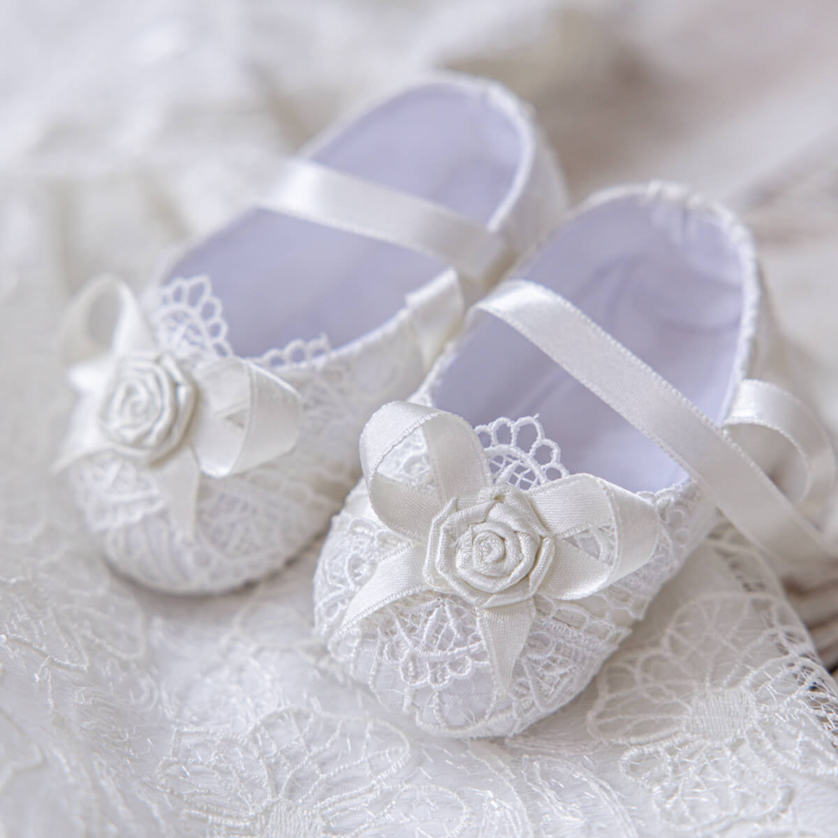 Christening Booties with lace and rose details on a white lace background