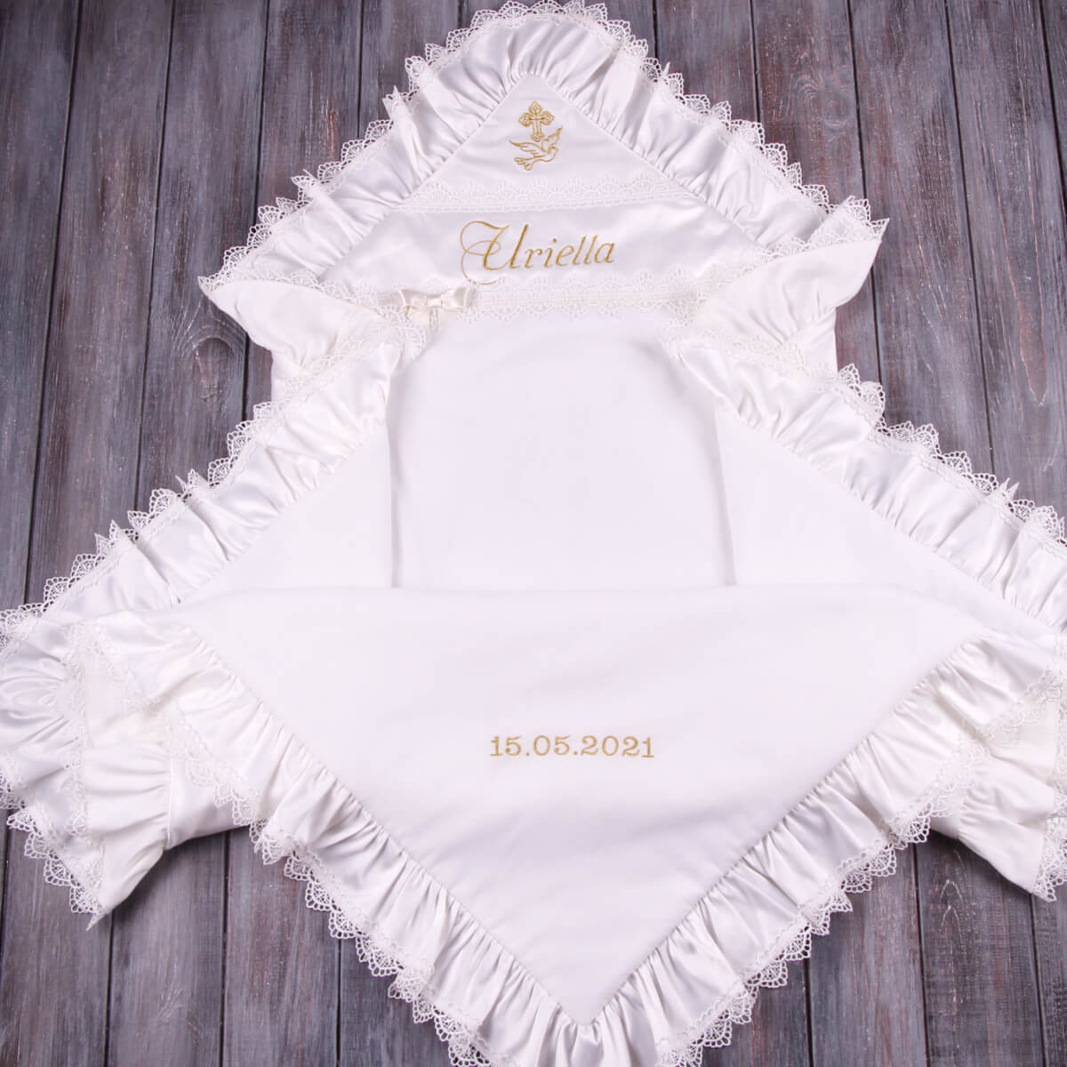 White embroidered baby blanket with lace trim on a wooden surface