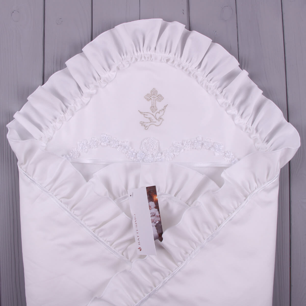 White embroidered baby blanket with a cross and dove design on a wooden surface