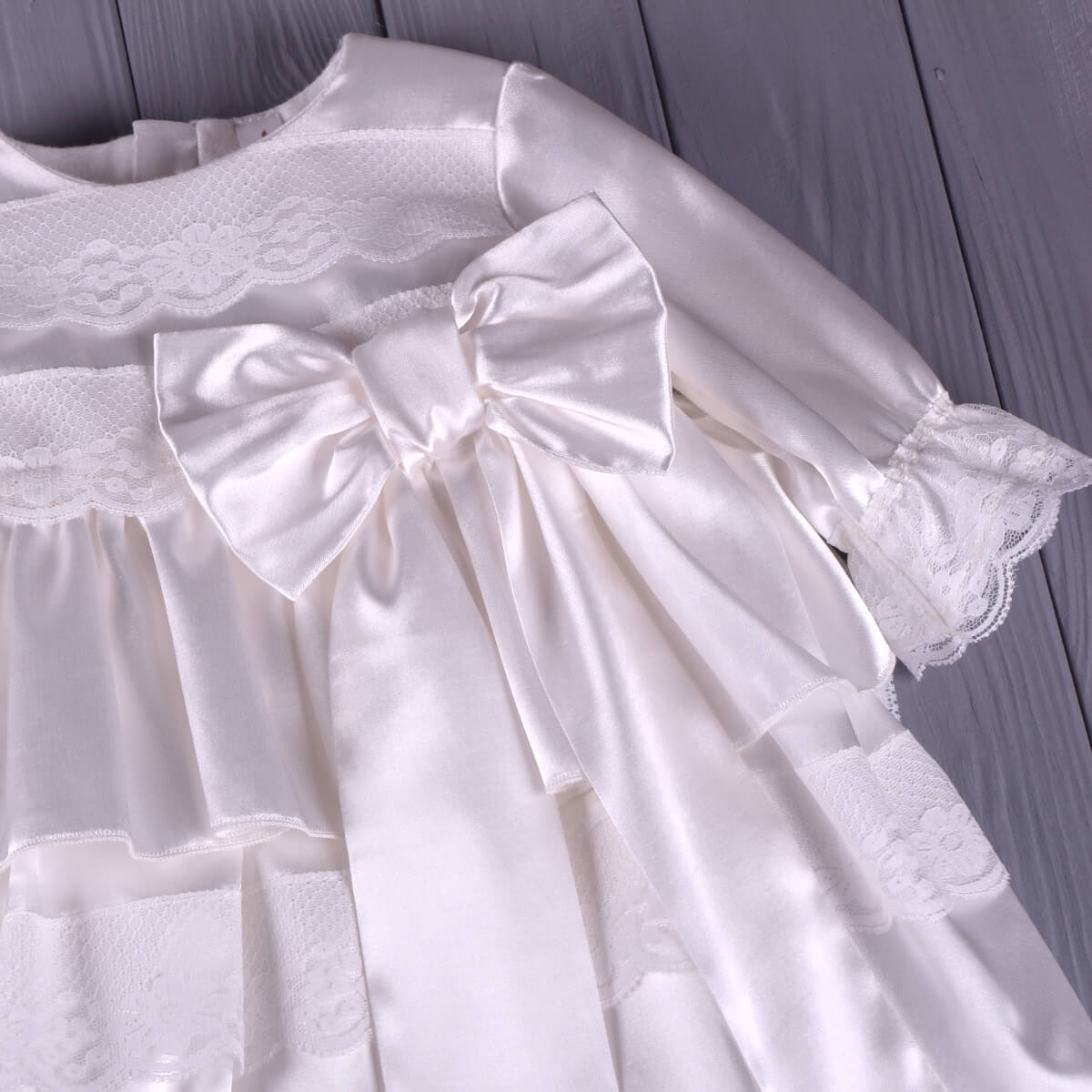 Baptism Gown Set with Hat for Girls – with a large bow on a wooden surface