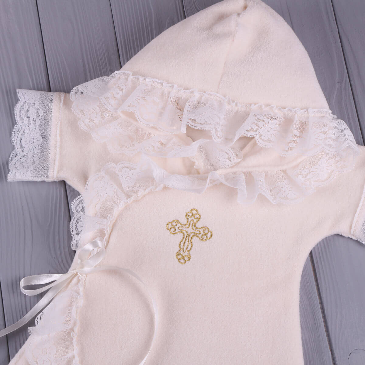 Baptism Gown with lace details and a gold cross on a wooden surface