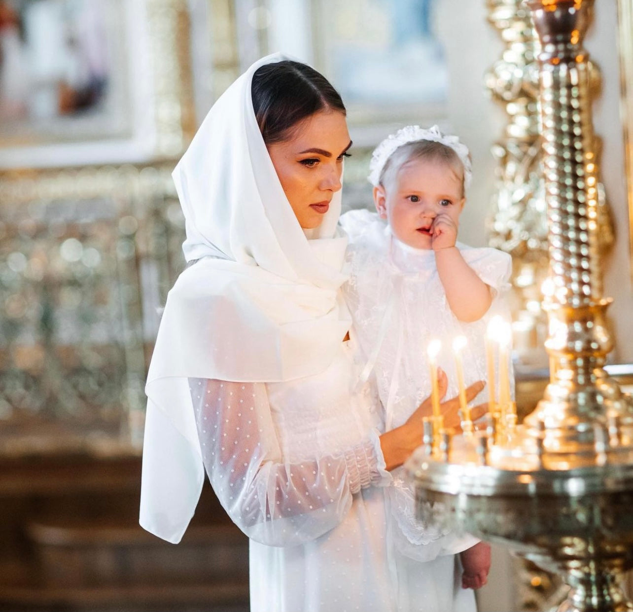 Woman in a Lace Baptism Gown Set with Bonnet for Girl  holding a child in a decorated indoor setting