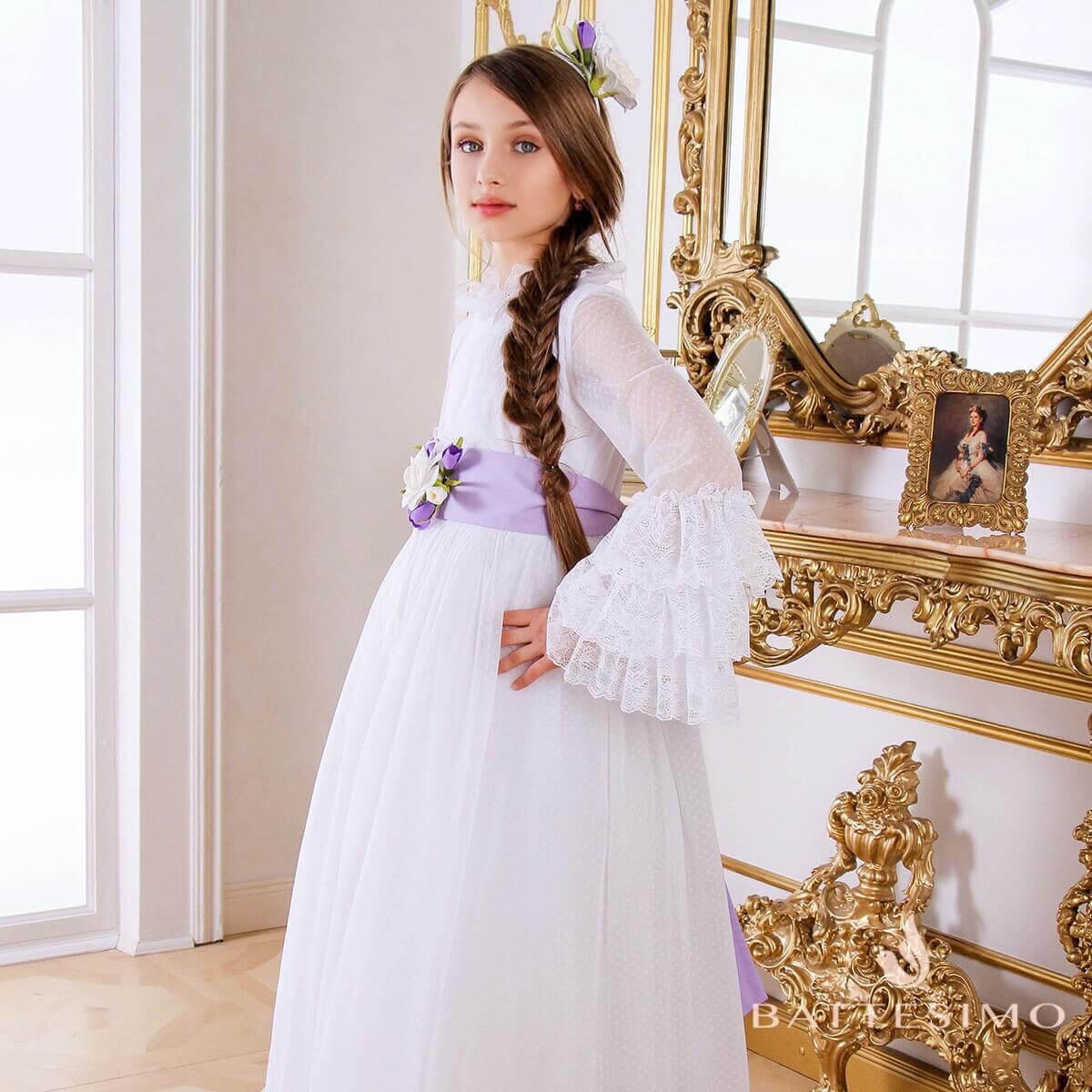 Young girl in Boho Chic Communion Dress with ruffled sleeves standing in front of a decorative mirror.