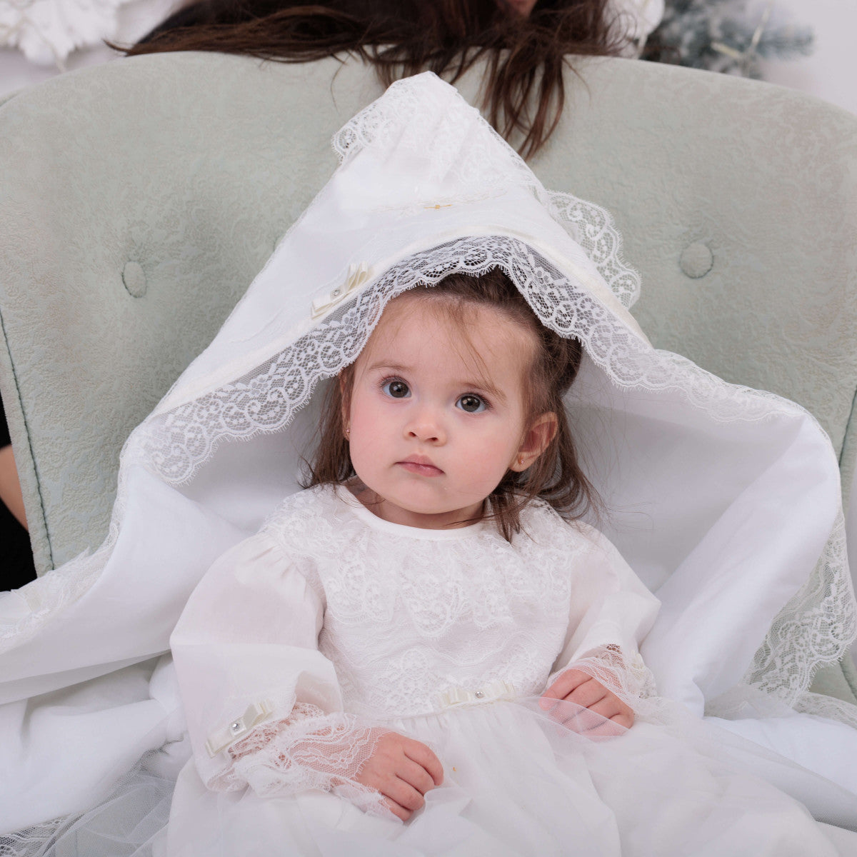 Child in a white dress with lace details sitting on a light green couch.