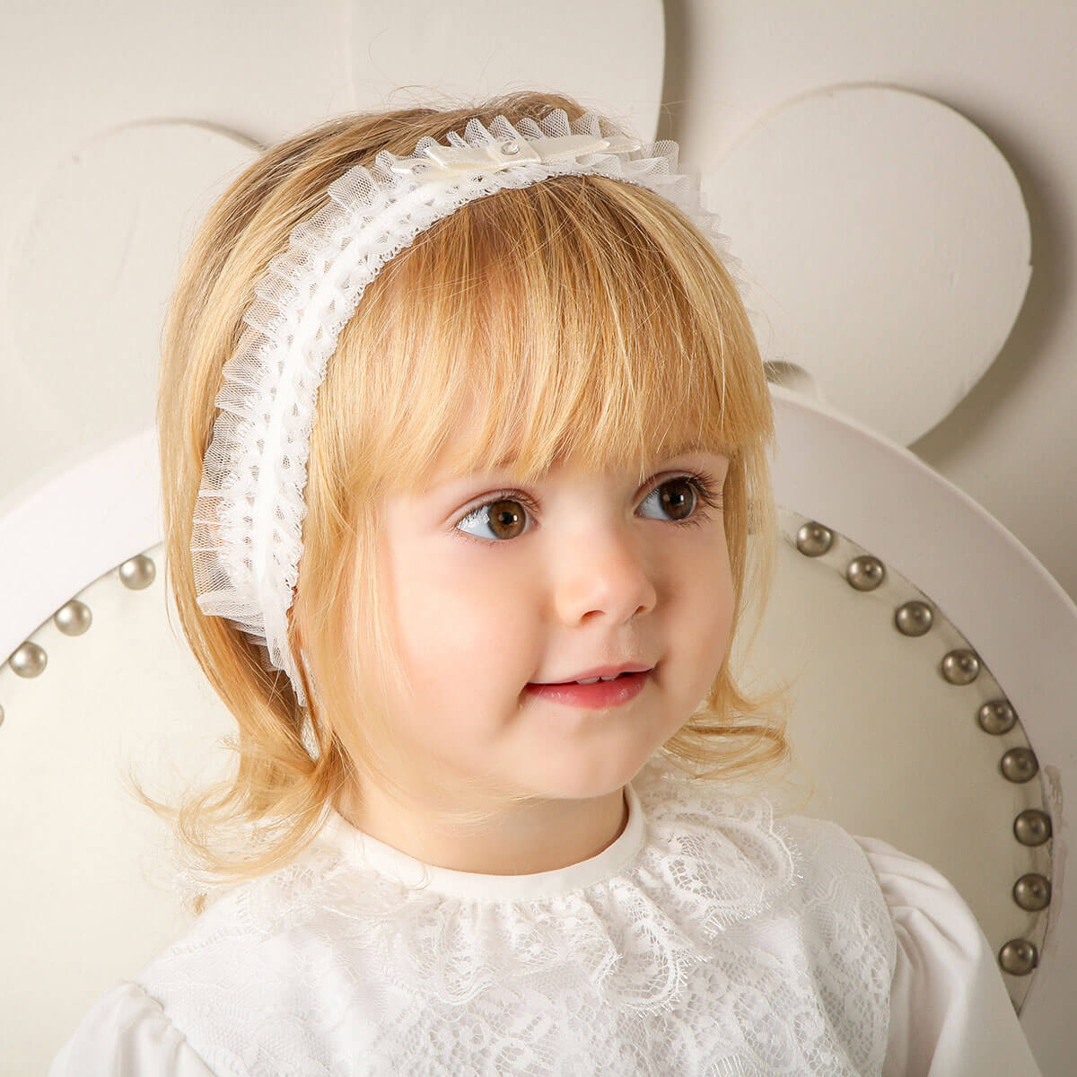 Young girl wearing the baby eadband and dress, sitting on a decorative chair.