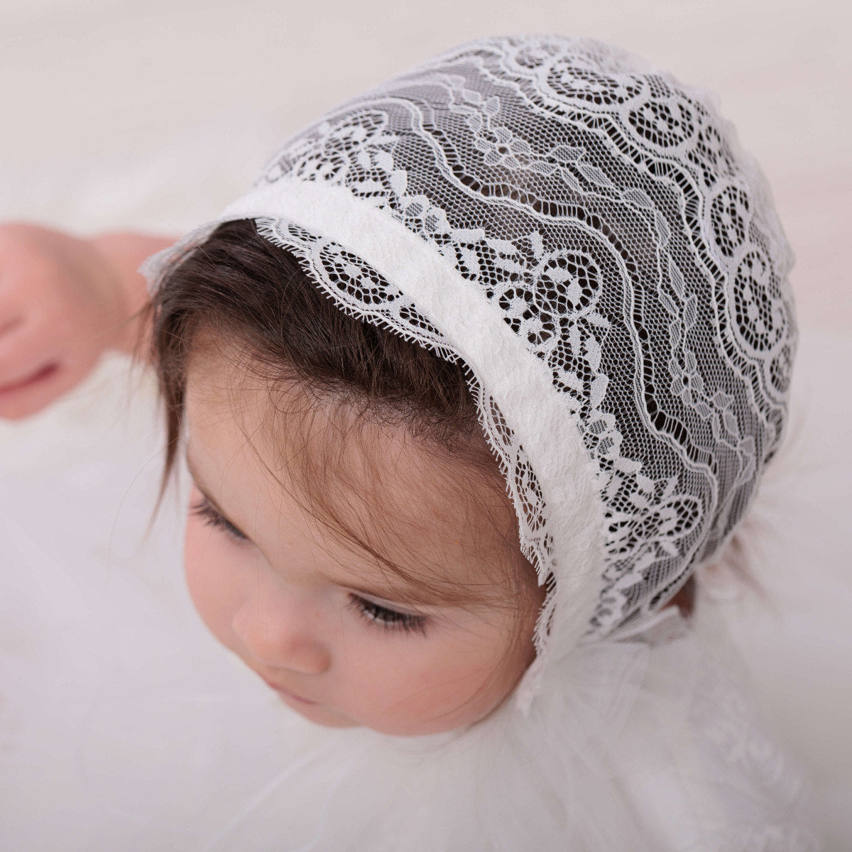 Baby wearing a  Lace Baptism Bonnet on a soft white background
