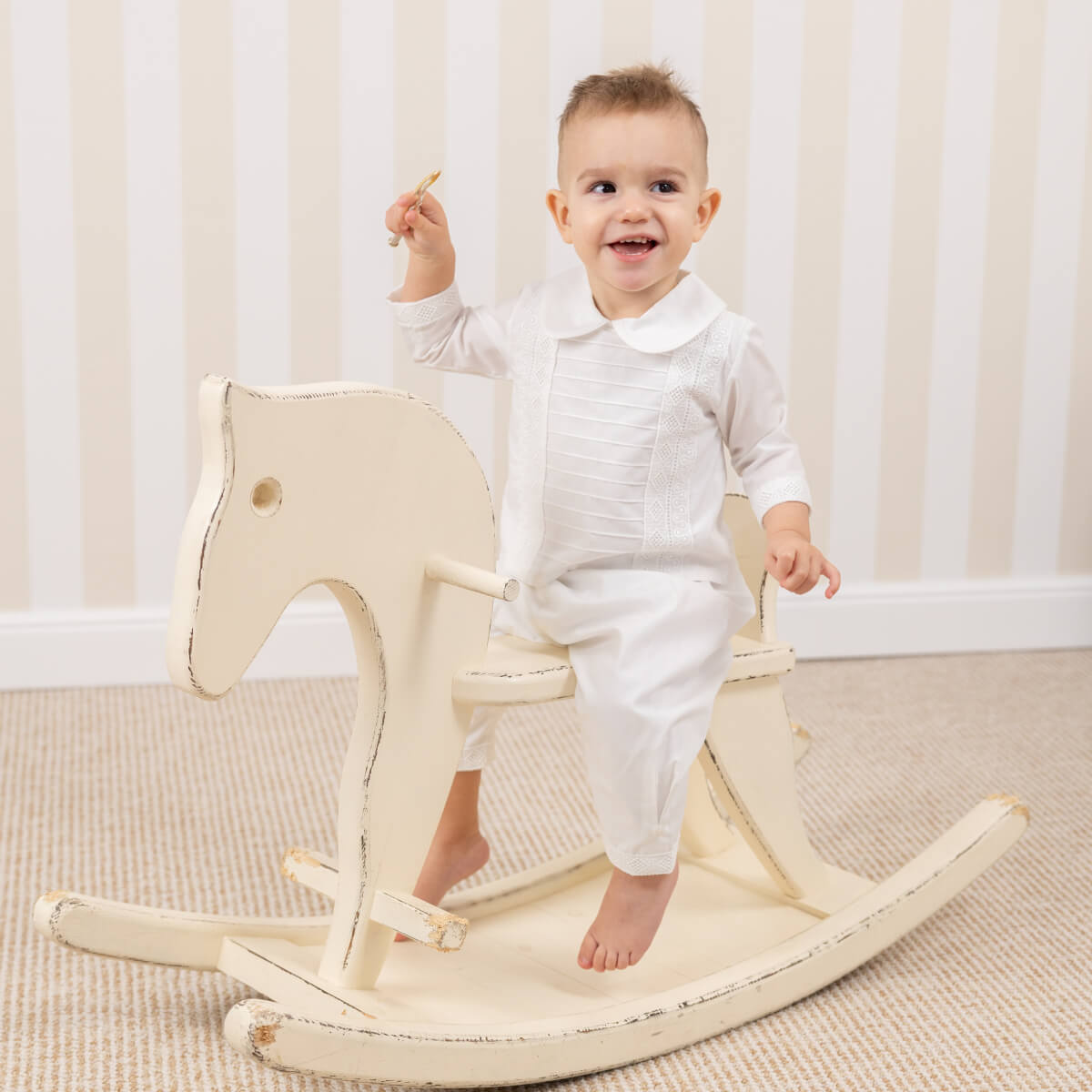 Child sitting on a wooden rocking horse in Baby Boy Baptism Suit.