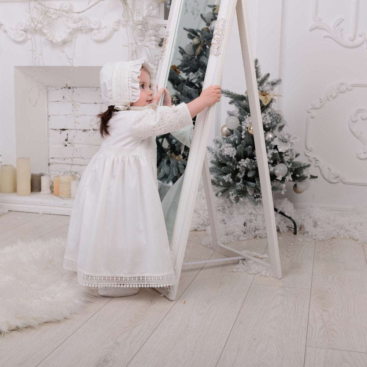 Girls Classic Christening Gown standing next to a Christmas tree in a decorated room.