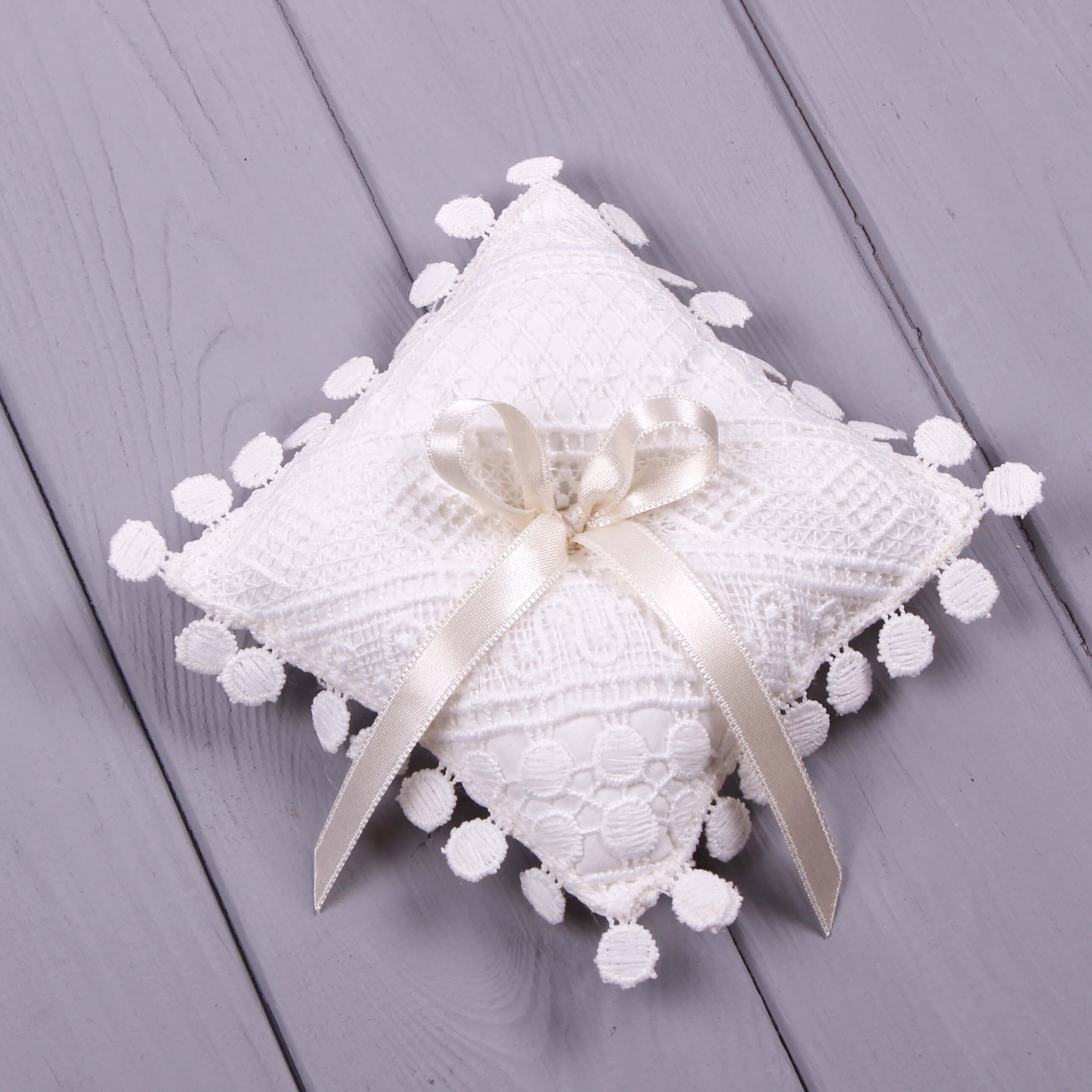 Baptism Ring Pillow  with pom-poms and a ribbon on a wooden surface