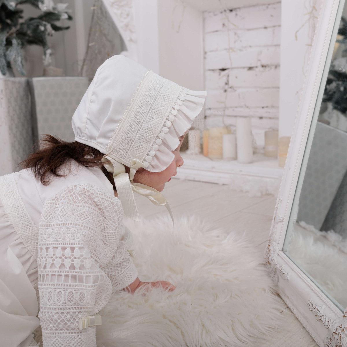 Person wearing a lace christening bonnet  a softly lit room with decorative elements.