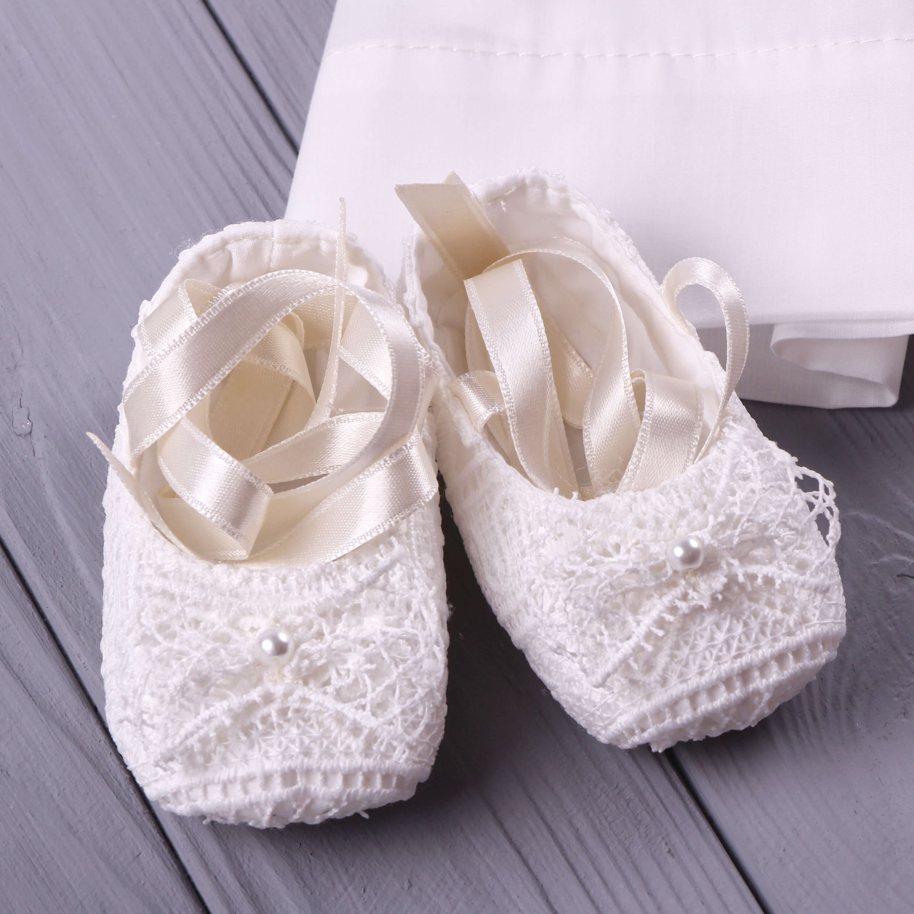 Baptism Booties with ribbons on a wooden surface