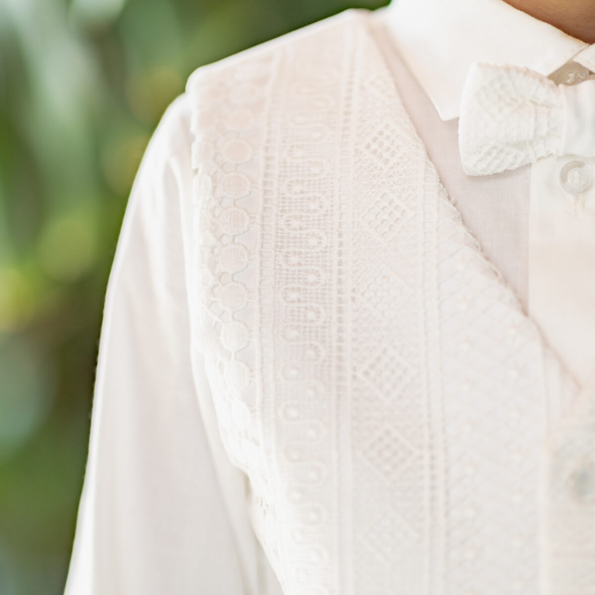 Close-up of a person wearing a light pink cardigan over a white shirt with a blurred green background