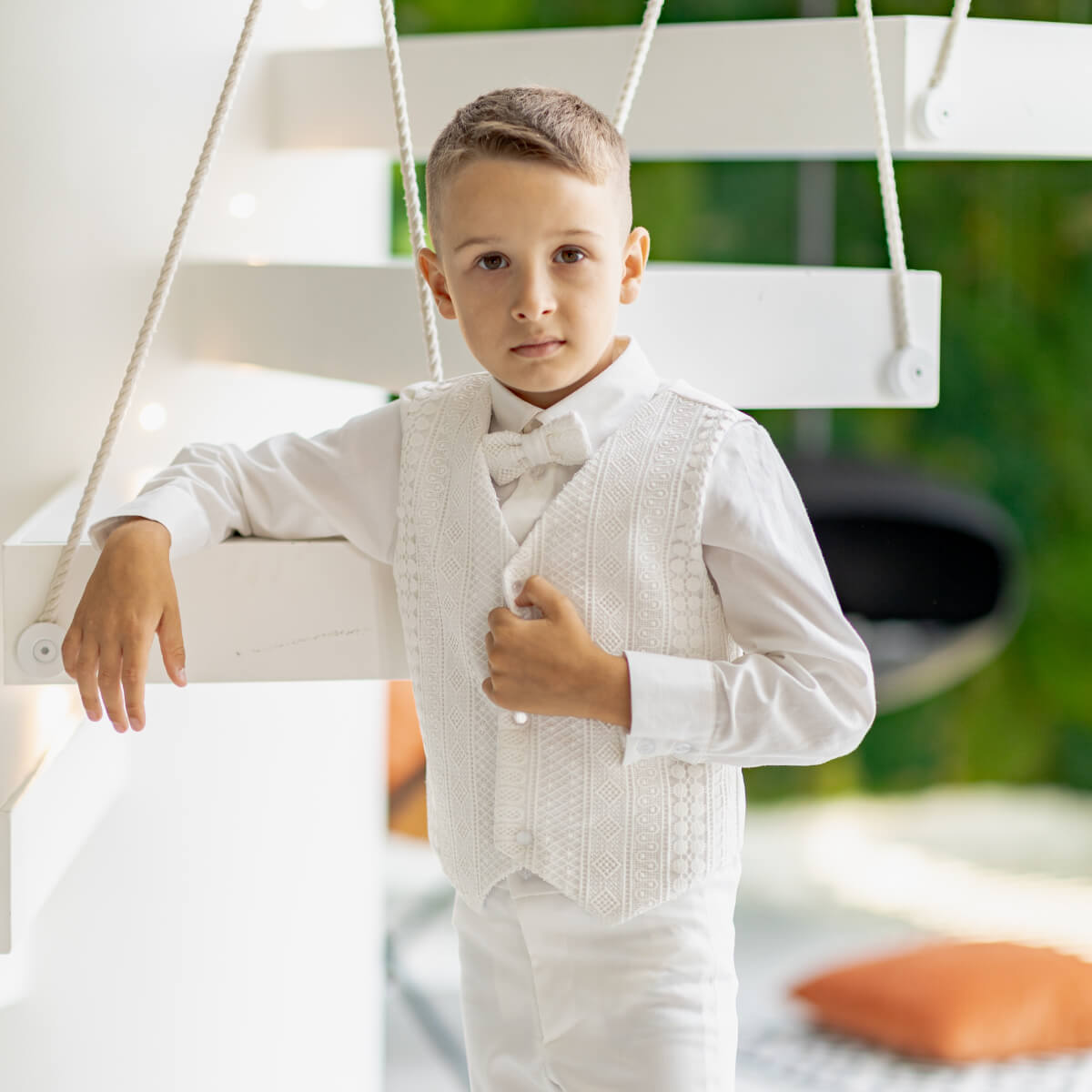 Young boy in a white suit standing on a swing with a blurred green background